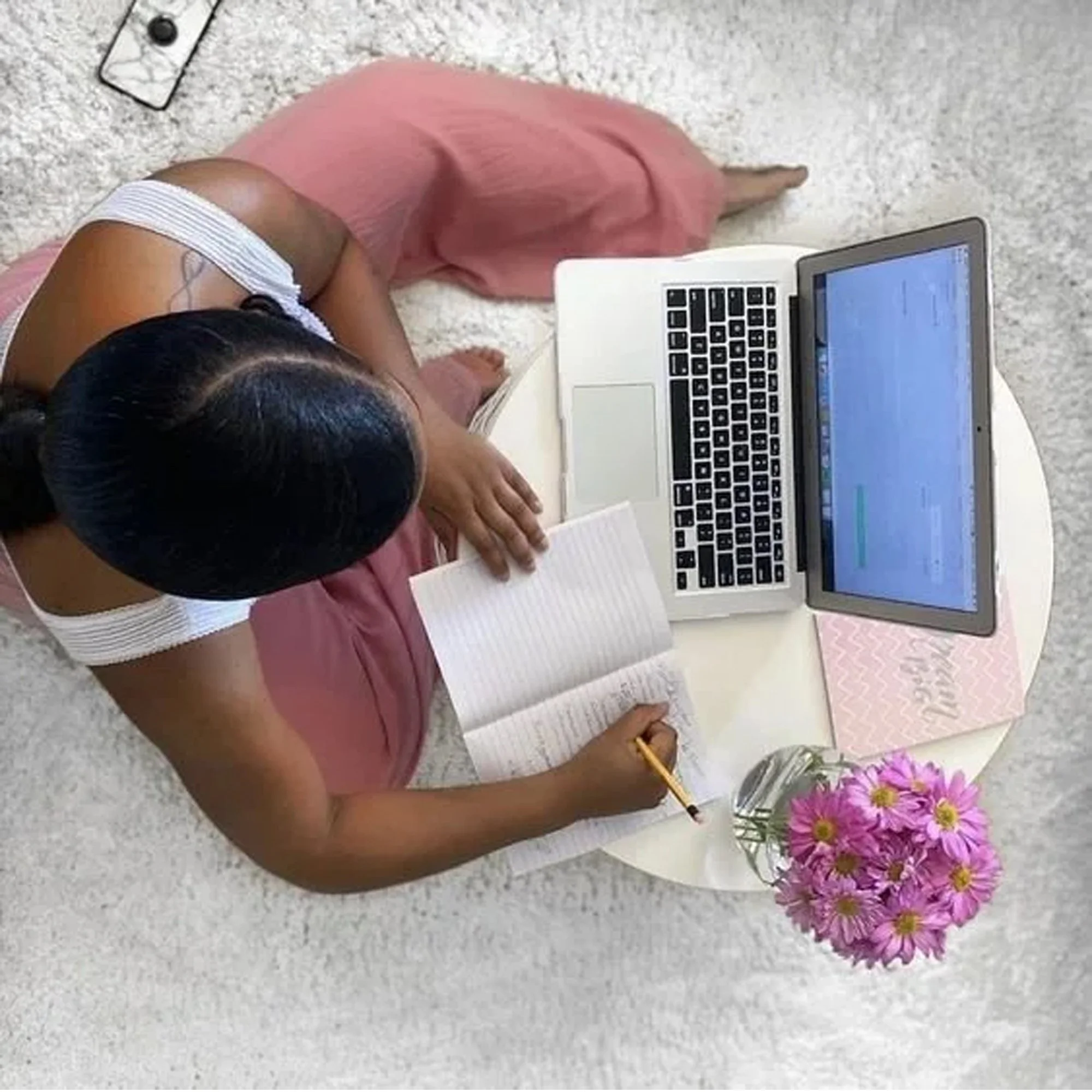 A woman content creator sitting on a pink blanket working on her laptop, planning her business finances, bookkeeping, and tax strategy with Fonville Financial & Tax Services.