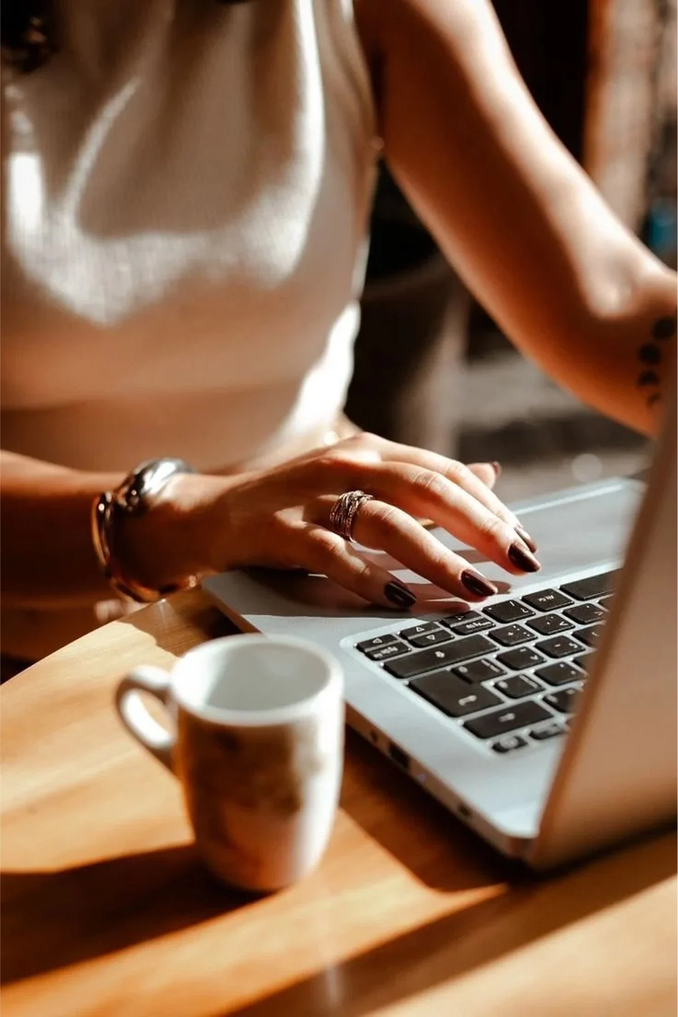 A woman freelancer working on her laptop with a coffee mug on a wooden table, managing cash flow, bookkeeping, and tax planning with Fonville Financial & Tax Services.