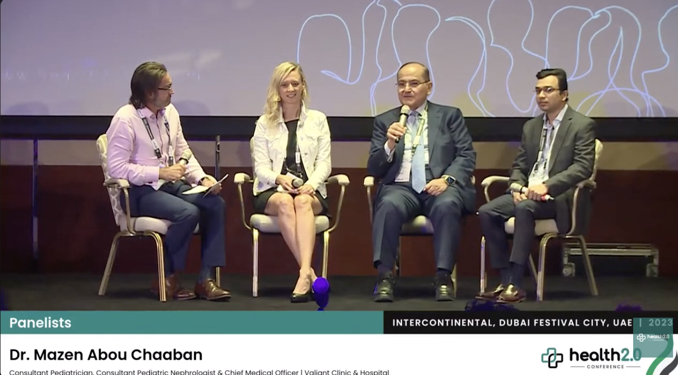 Five panelists sitting on stage at a conference, with a large screen behind them displaying text. The panel includes Dr. Mazen Abou Cheaban, a pediatrician, nephrologist, and medical officer, participating in a discussion at the Health 2.0 Conference in Dubai, 2023.
