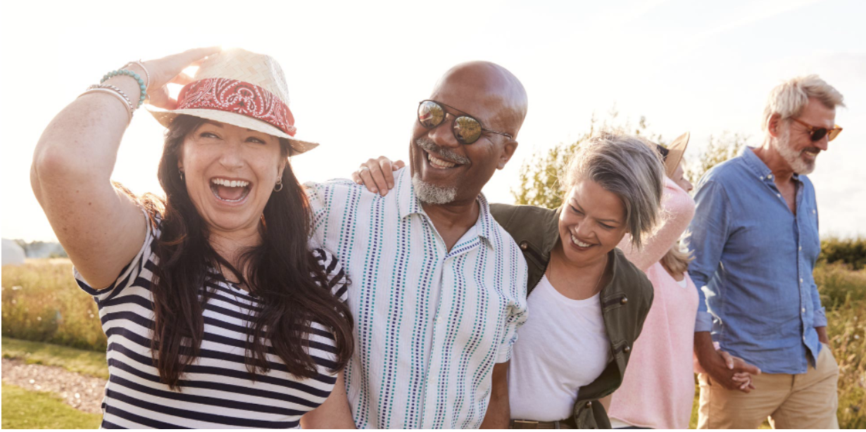 Fünf Menschen lachen und halten sich an den Händen im Freien bei Sonnenuntergang, umgeben von Natur.