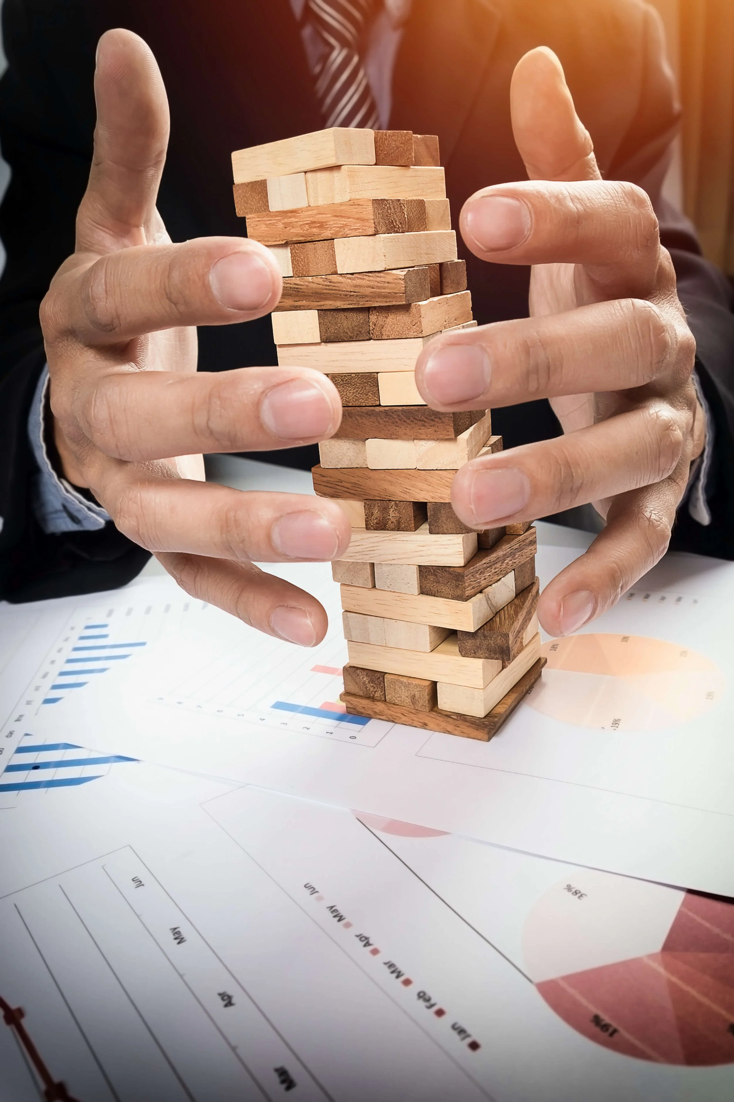 Hands protecting a wooden tower from collapsing, illustrating cost minimisation and risk management in business