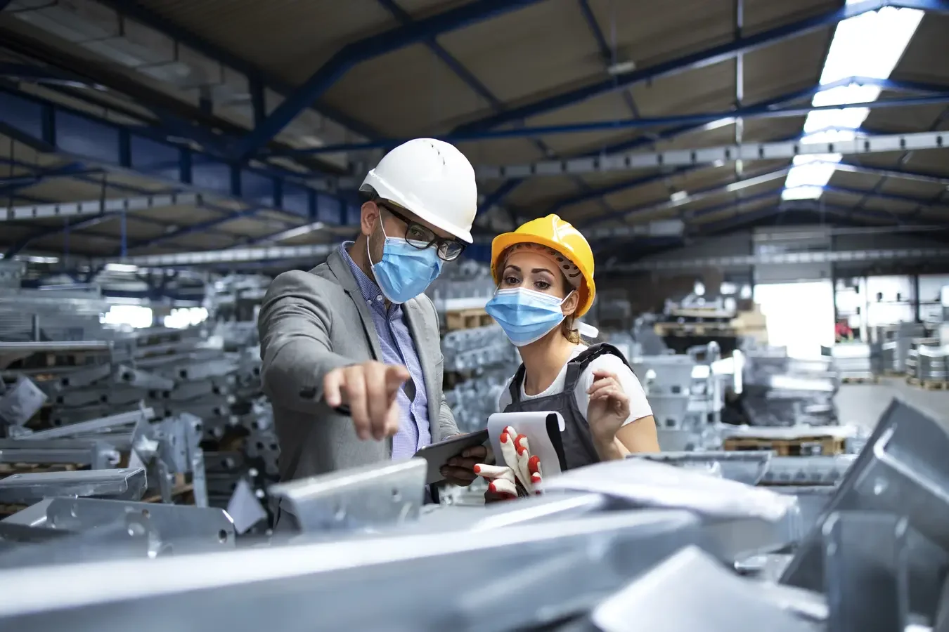 Two industrial workers discussing a manufacturing fabrication process while wearing helmets and protective masks