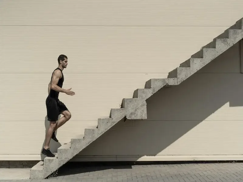 A man in athletic clothing running up outdoor concrete stairs with wall background and shadow.