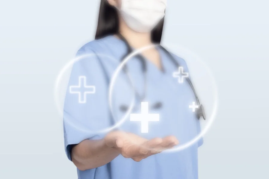 Healthcare professional in blue scrubs and a white mask, with a stethoscope around her neck, extending her hand with digital health graphics, including plus signs, over her hand.
