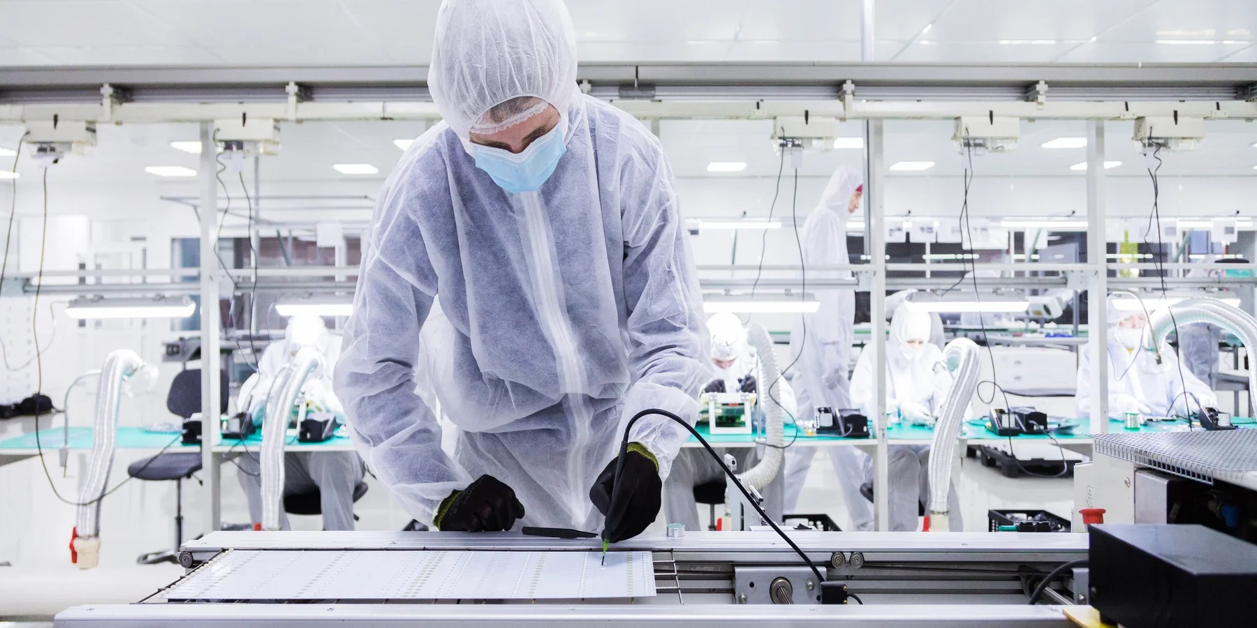 Workers in full protective gear working in a cleanroom assembly line, handling electronic components.