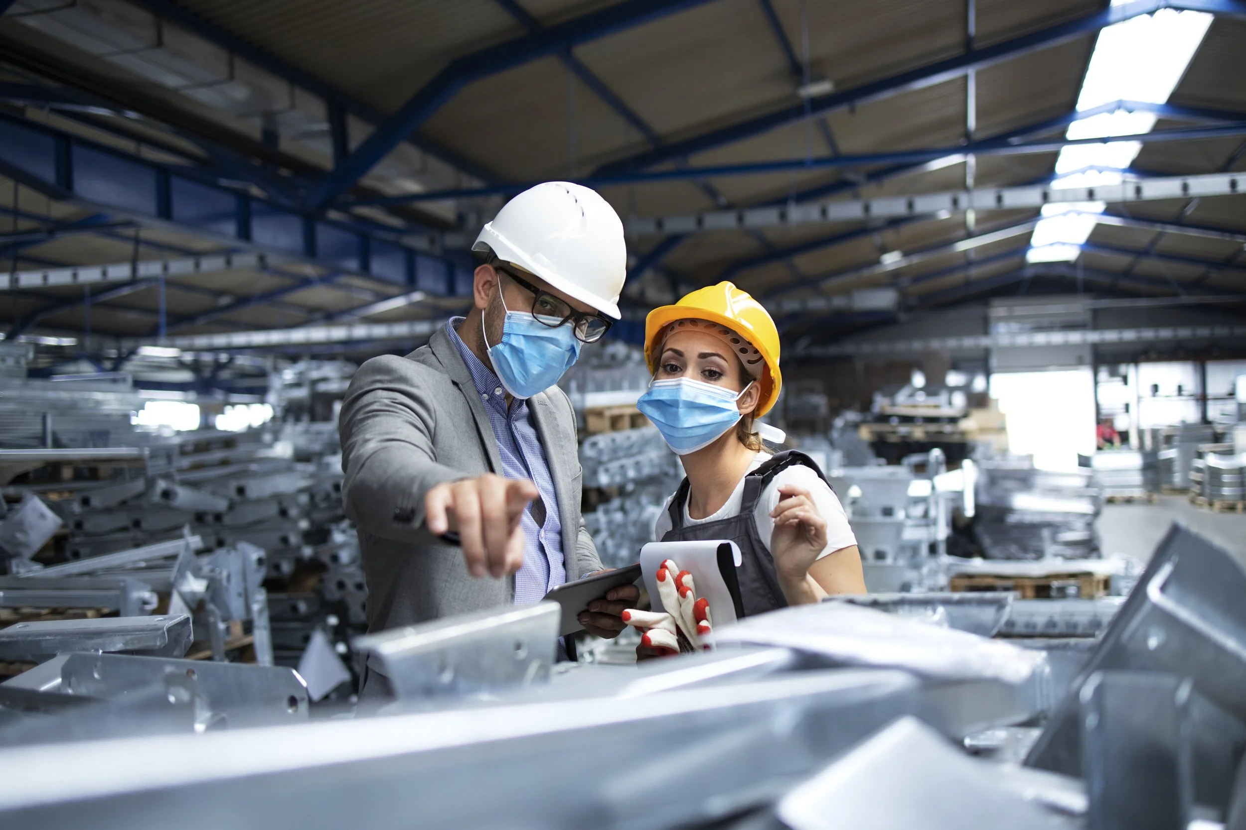 Two industrial workers discussing a manufacturing fabrication process while wearing helmets and protective masks