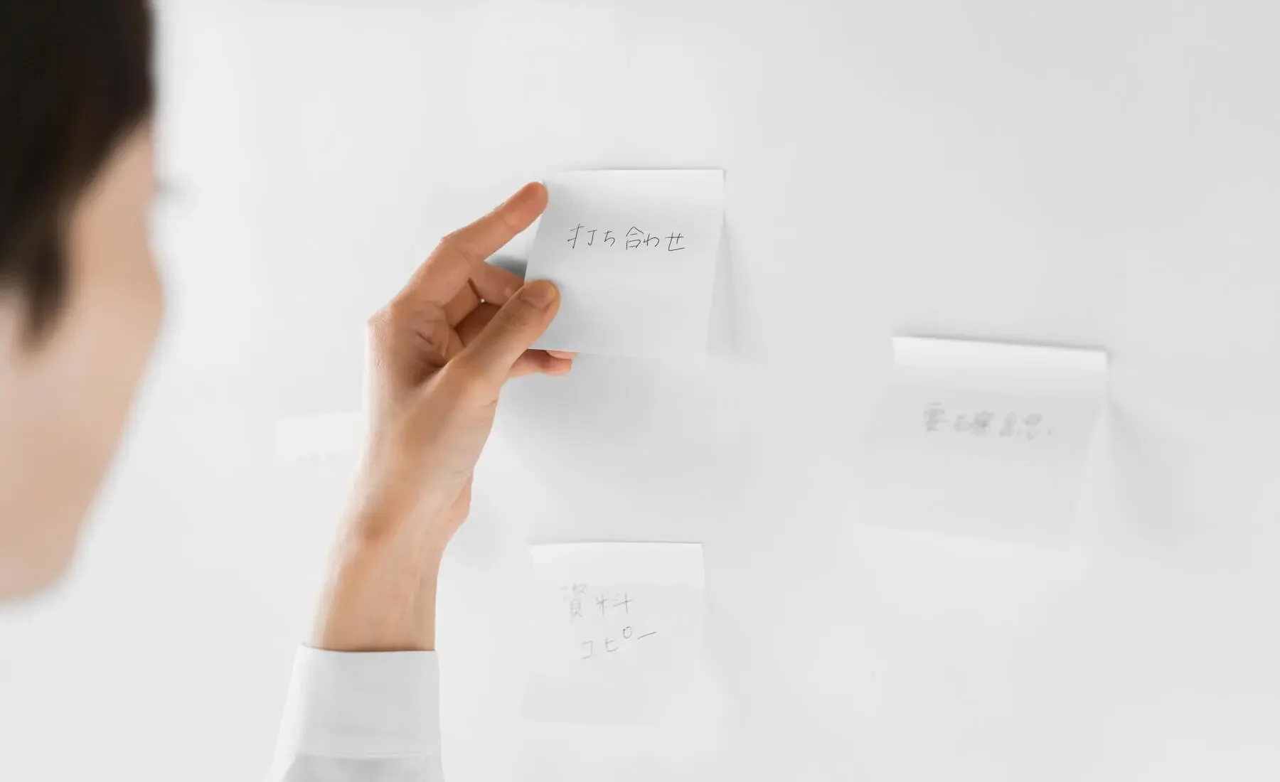 A person sticking a note with Japanese characters onto a white wall, others are already attached.