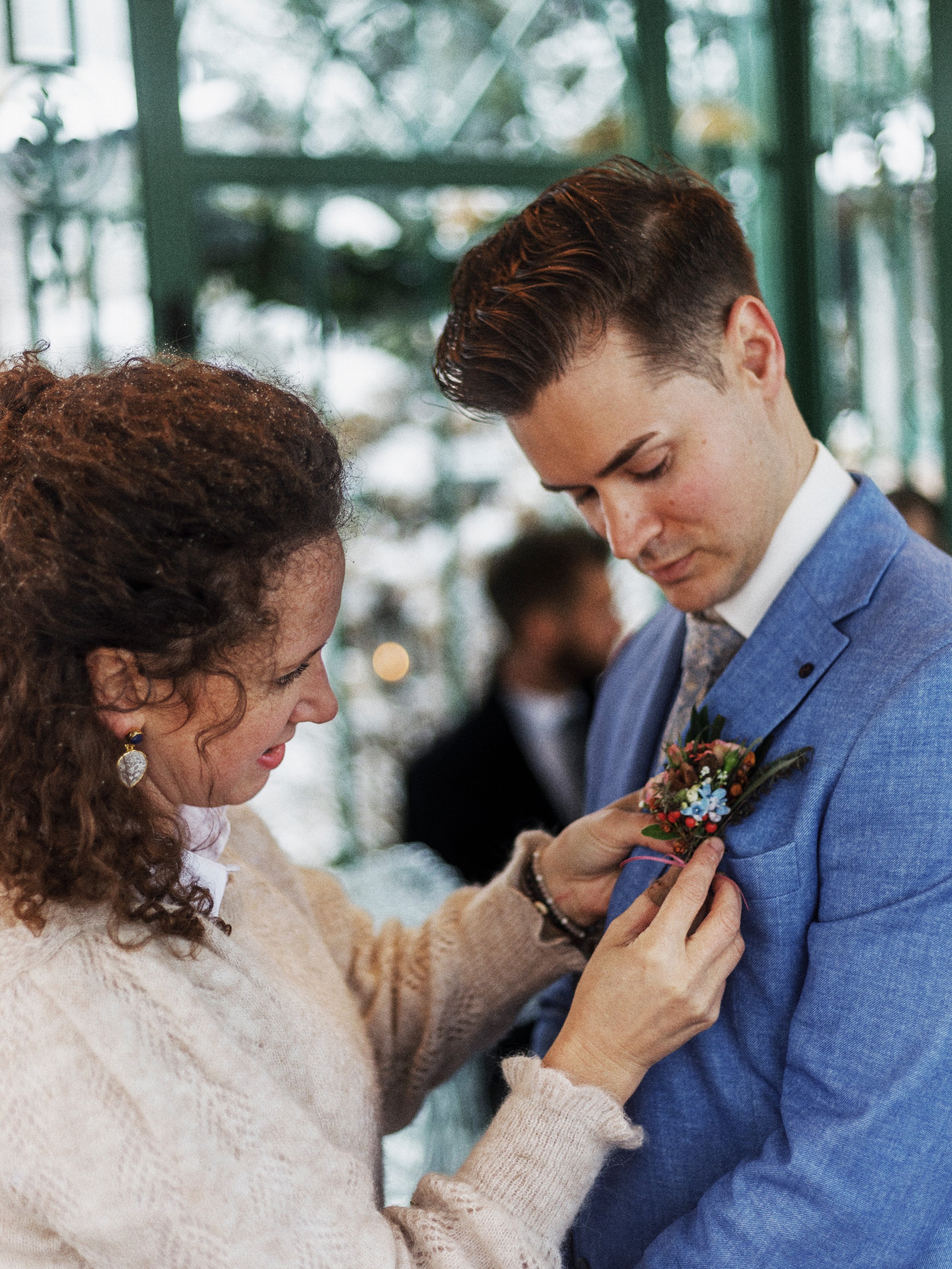 Eine Frau steckt einem jungen Mann einen Blumentill darstellen bei einer formellen Veranstaltung in einem Glasgebäude.