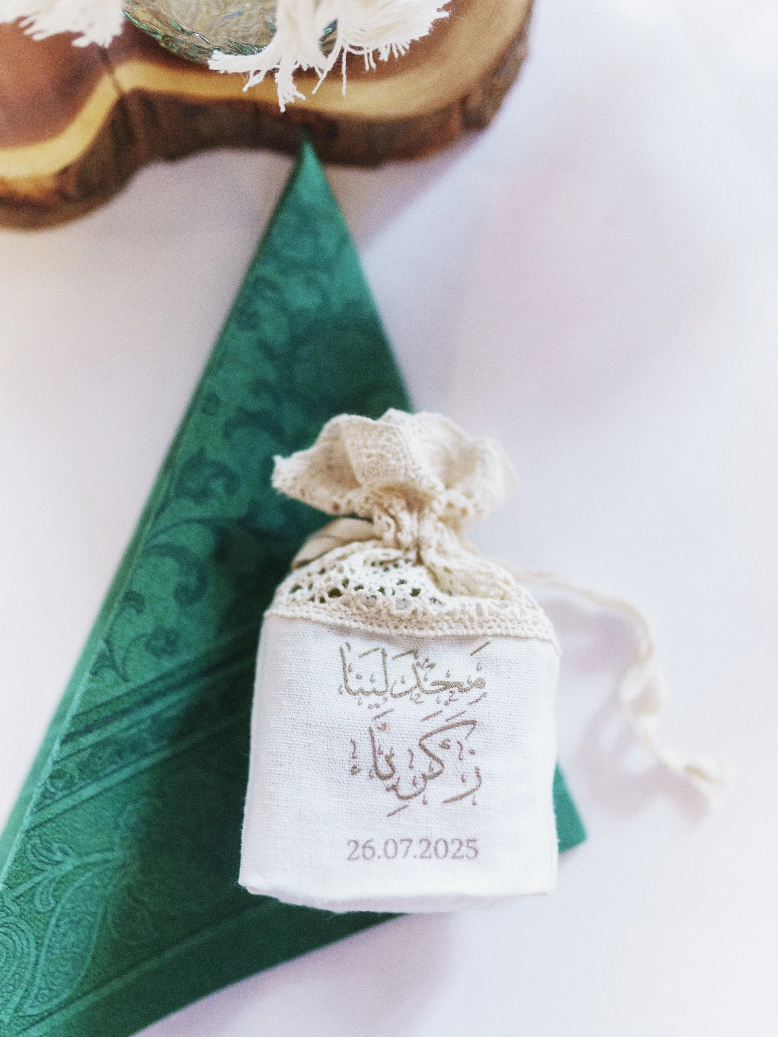 Ein kleines weißes Säckchen mit arabischer Schrift und Datum, das an einer grünen Dekoration hängt.