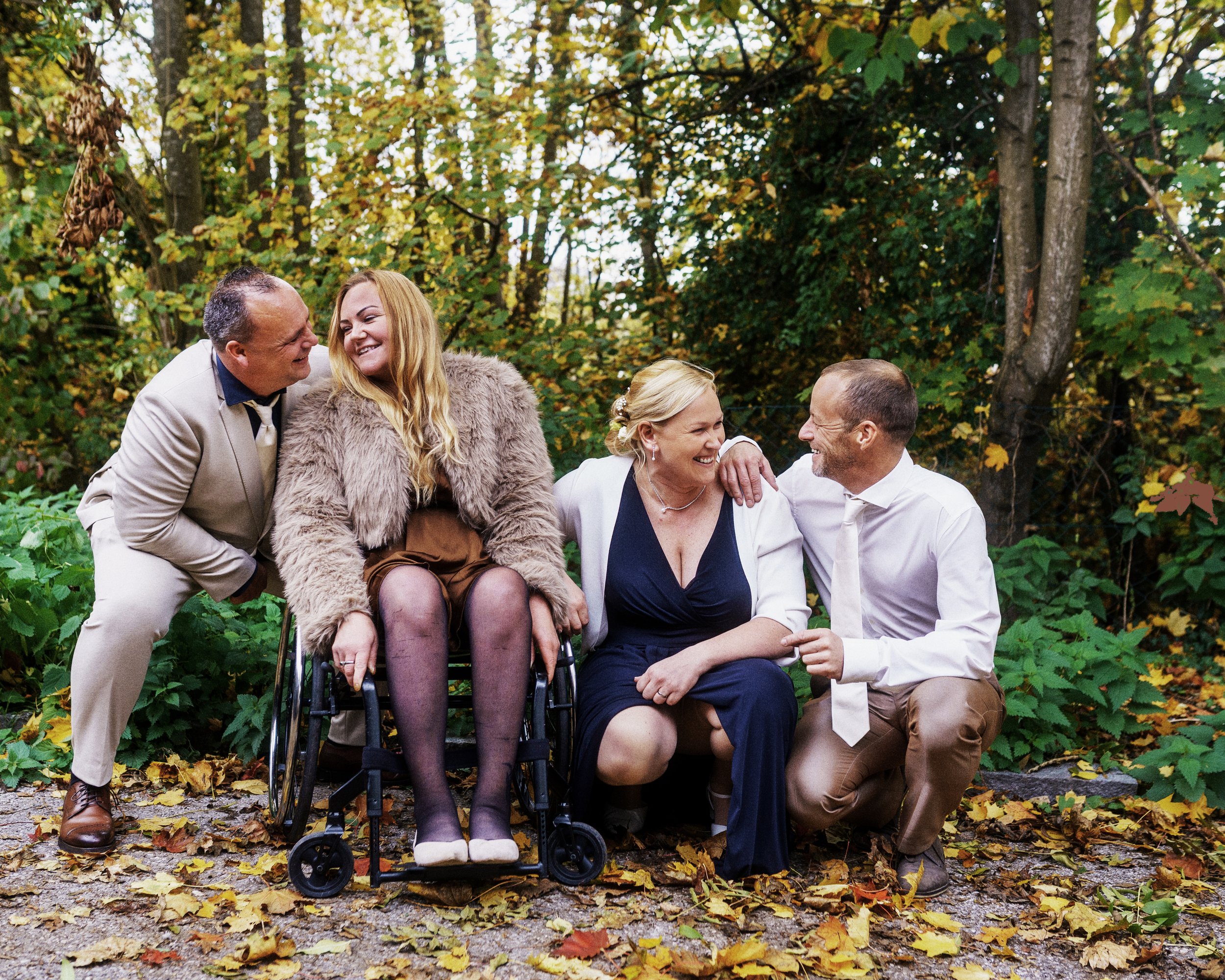 Vier Menschen lachen und unterhalten sich im Park, umgeben von Herbstbäumen und Laub auf dem Boden, bei einer positiven Zusammenkunft im Freien.