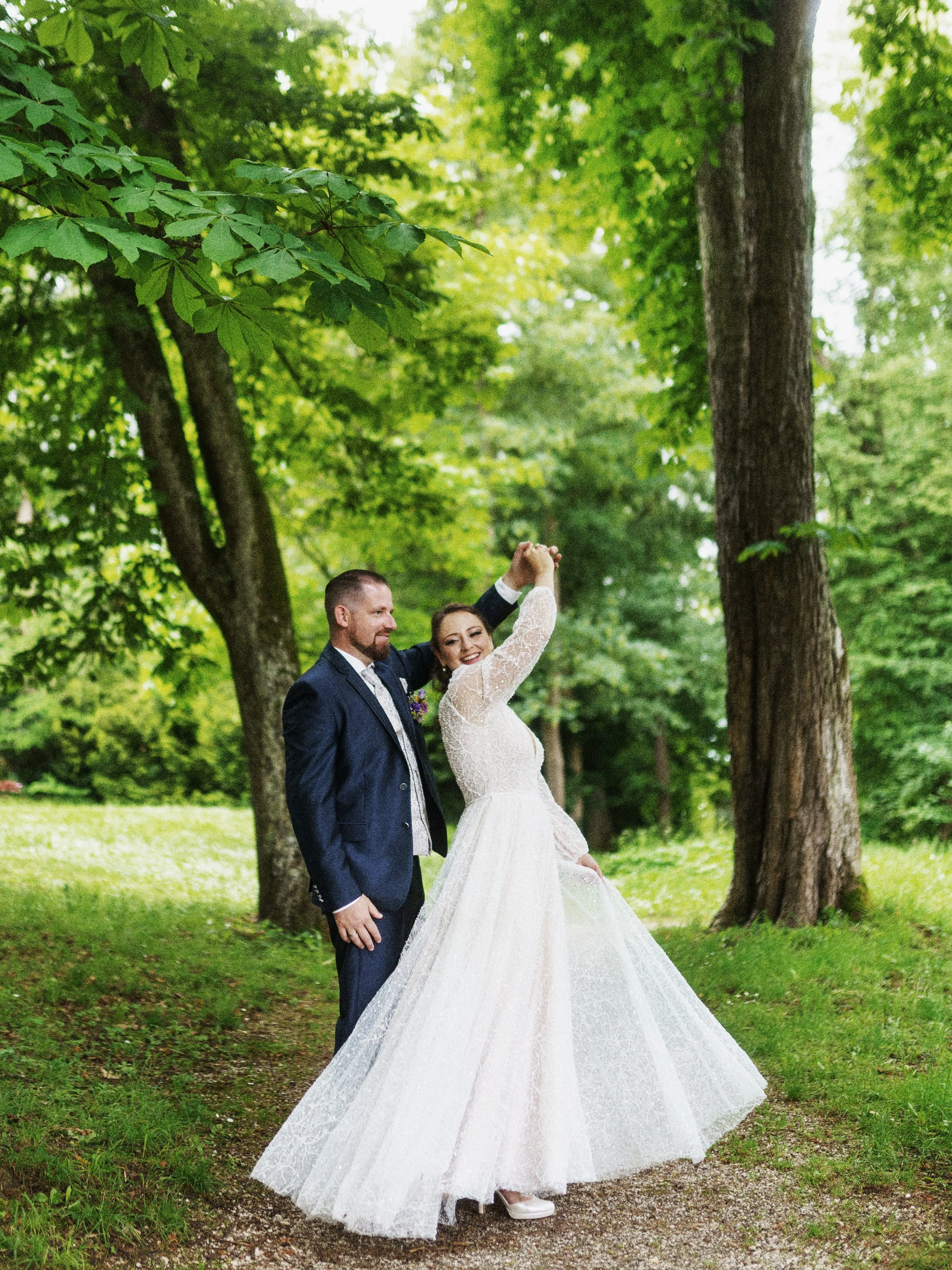 Ein Brautpaar tanzt im Grünen, umgeben von Bäumen, bei einer Hochzeitsfeier im Freien.