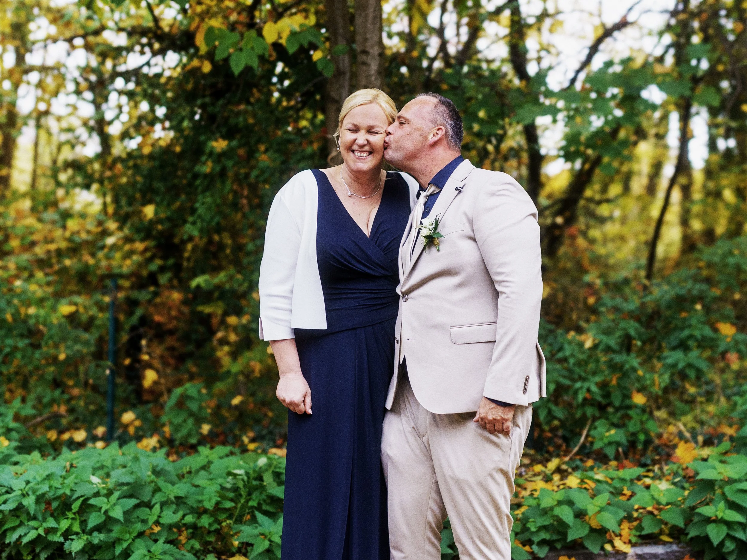 Eine Frau im Brautkleid und ein Mann im Anzug küssen sich in einem Wald bei einem Hochzeitsshooting.