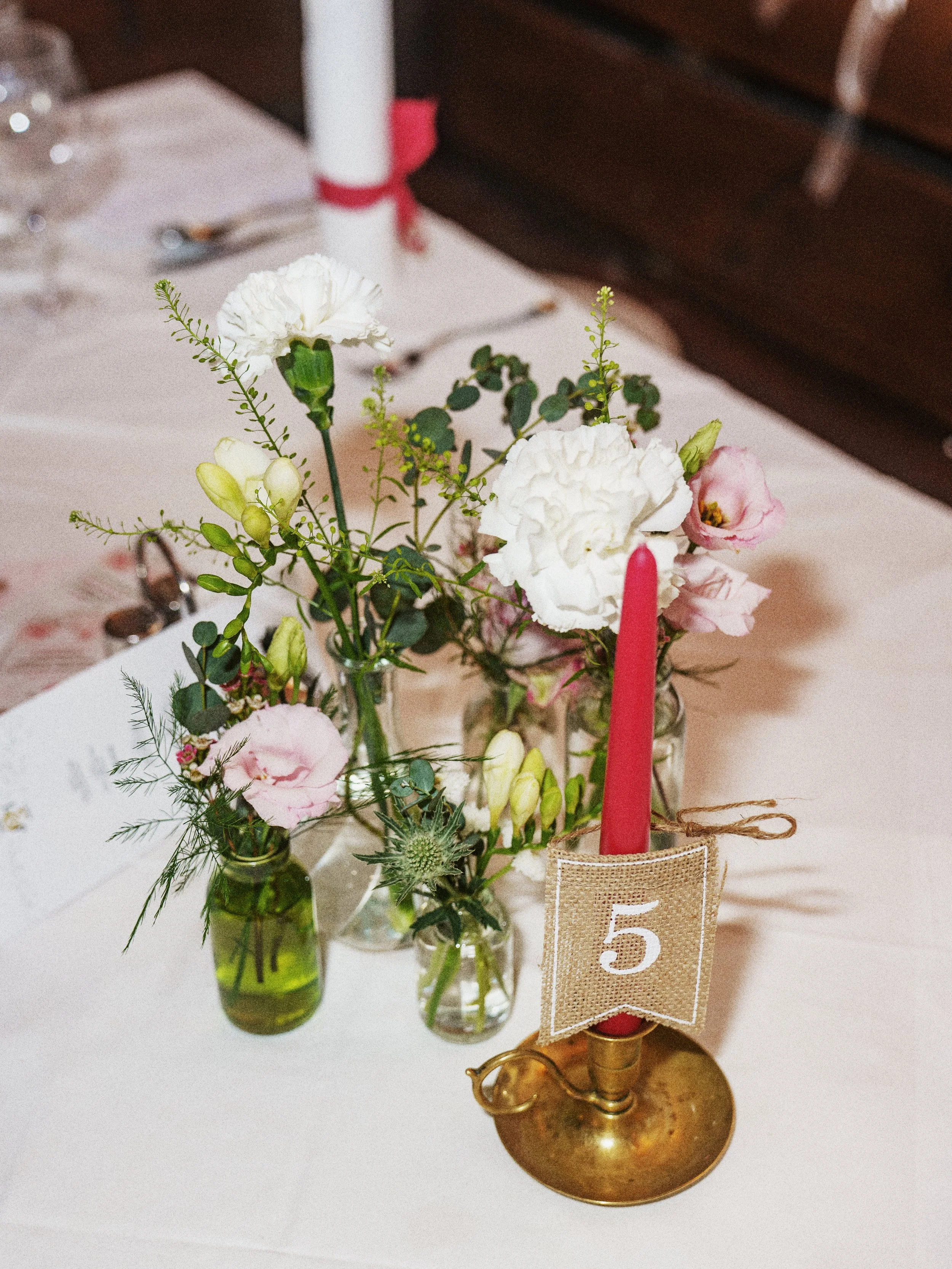 Mittagstisch mit Blumenstrauß in kleinen Gläsern, rote Kerze mit Nummer 5, auf einem festlichen Tisch.