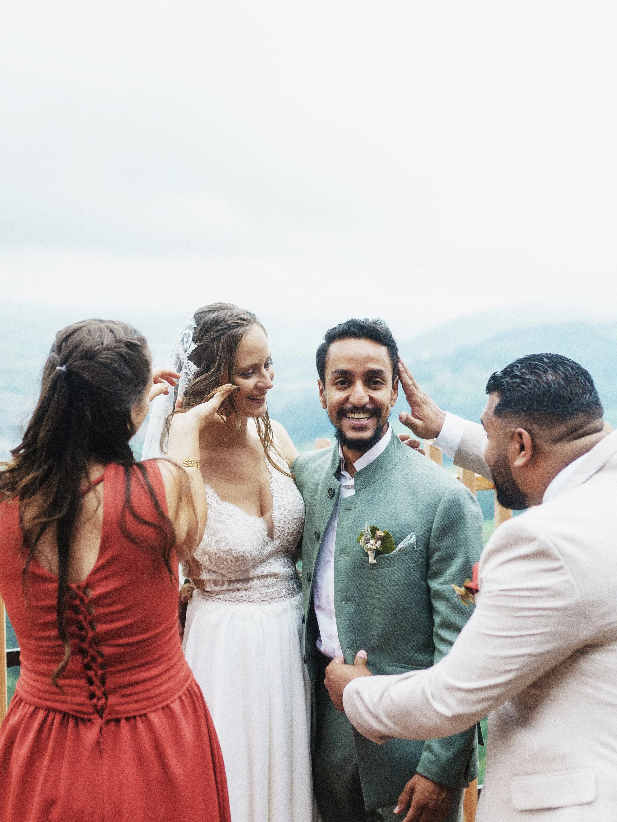 Eine Hochzeit im Freien mit einem lachenden Brautpaar und drei Freunden, die die Stimmung auf einem Berggipfel genießen.