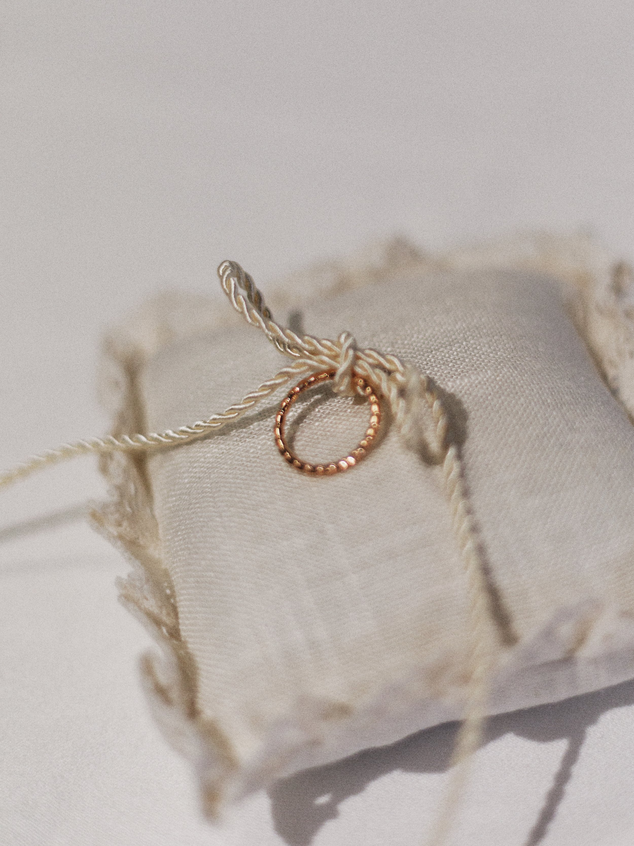 Rosa-goldenene Halskette mit kleinem Ring auf einem weißen Stoffkissen