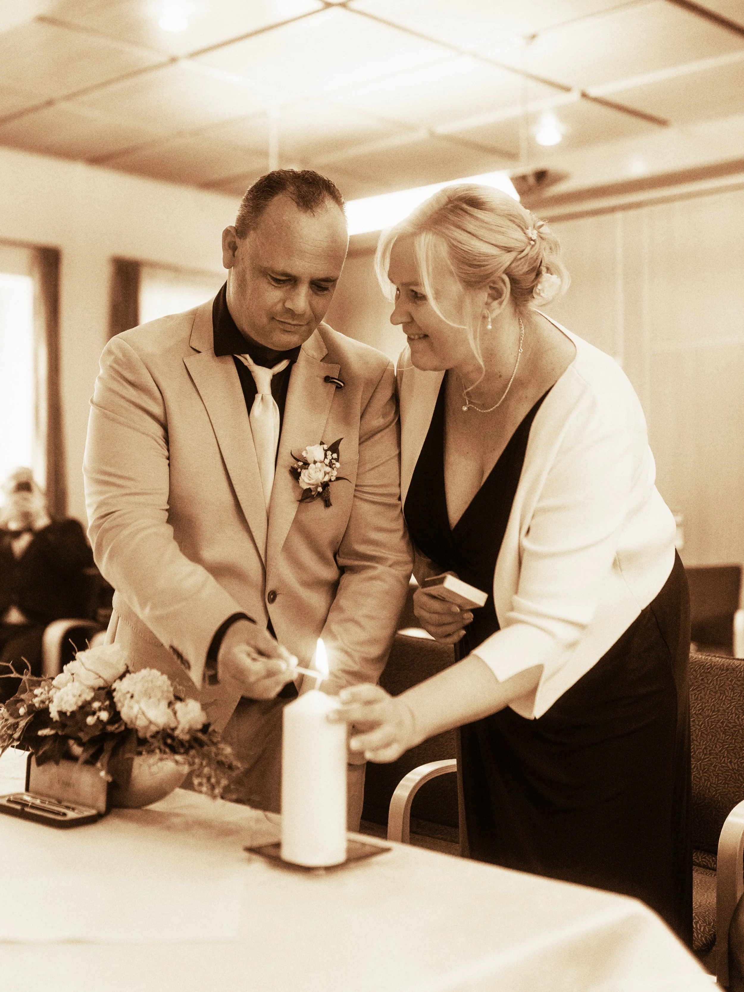 Zwei Menschen, ein Mann und eine Frau, bei einer Zeremonie, die eine Kerze anzünden, in einem Raum mit gedämpftem Licht.