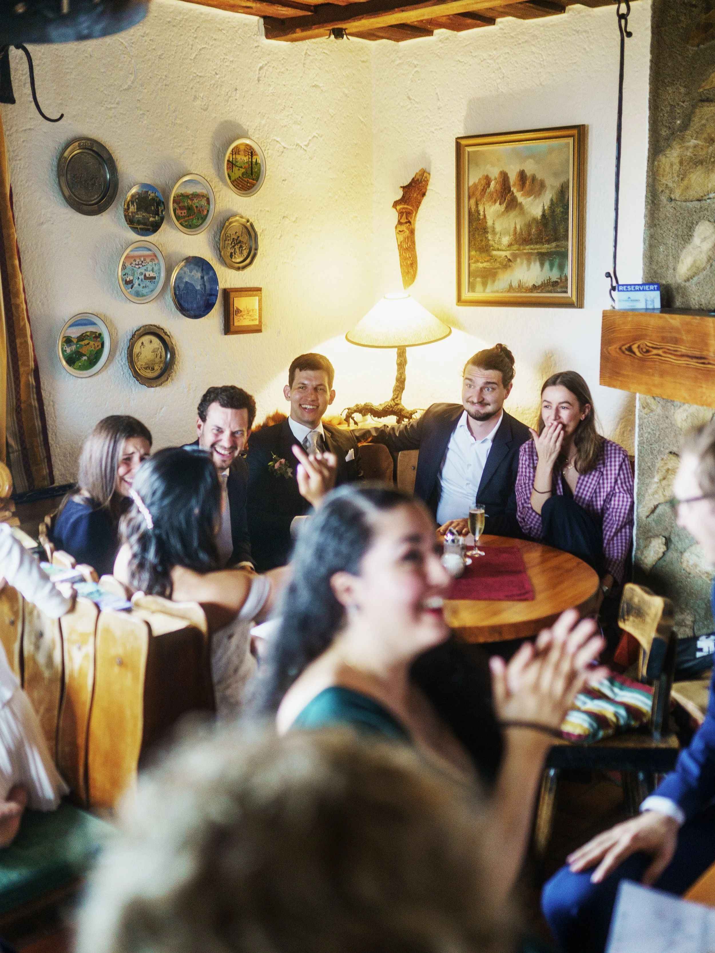 Menschen feiern fröhlich in einem gemütlichen Raum mit Holzdekoration, Wandbildern und warmem Licht.