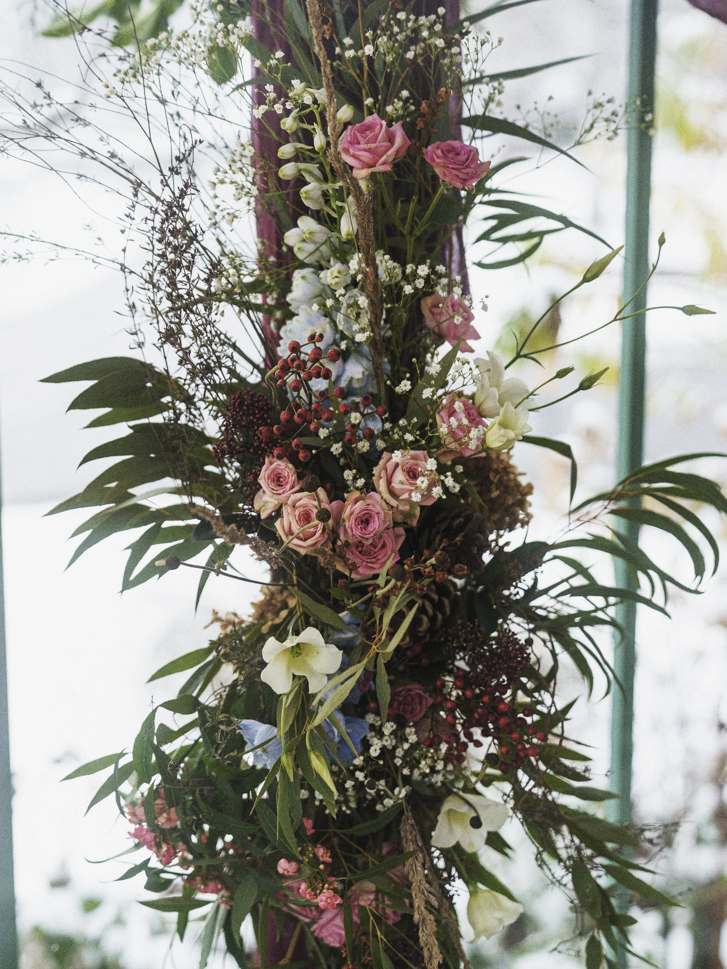 Blumengesteck mit rosa Rosen, weißen Lilien, Schleierkraut und grünen Blättern.