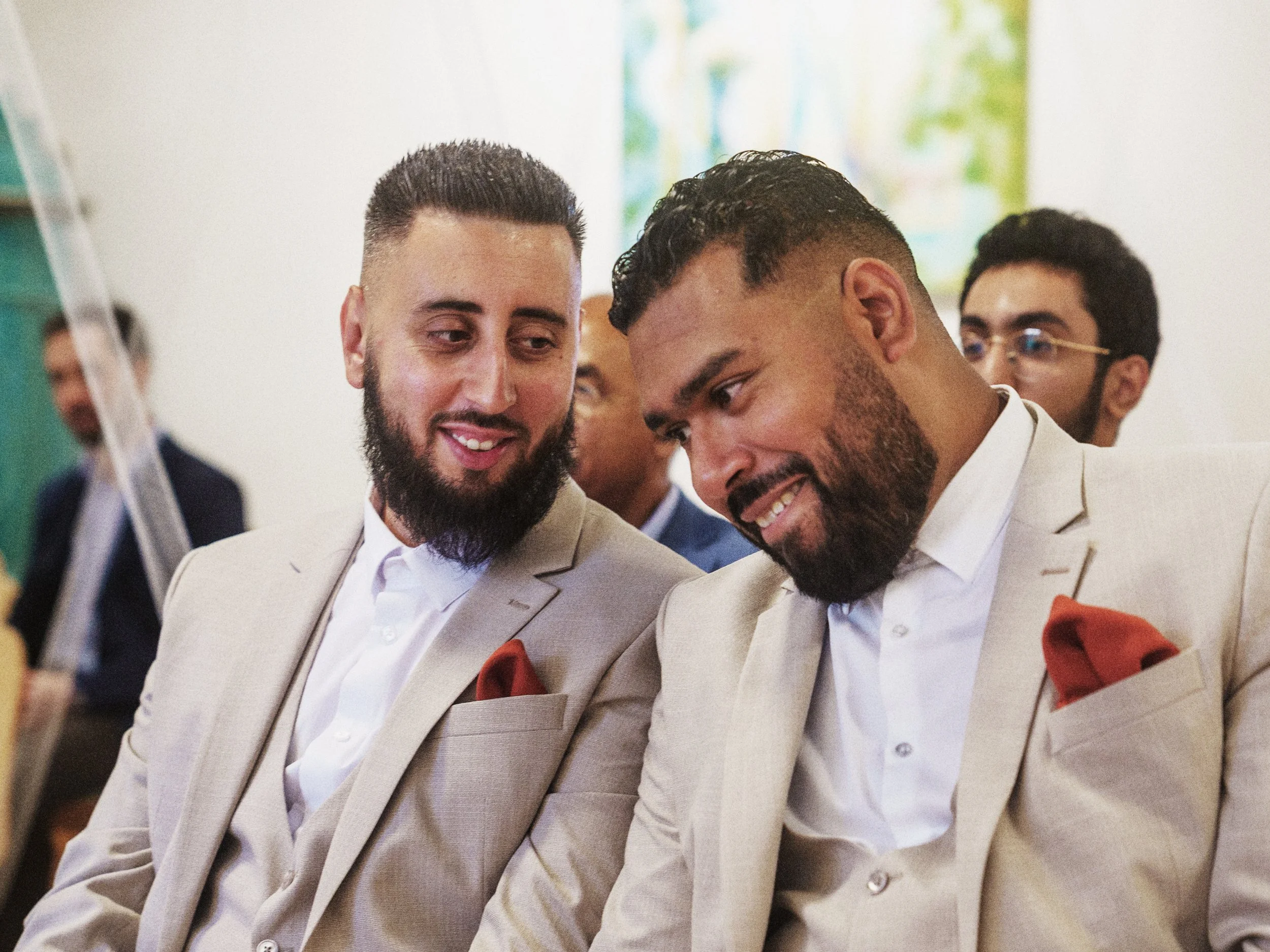 Zwei Männer in beige Anzügen lächeln sich an.