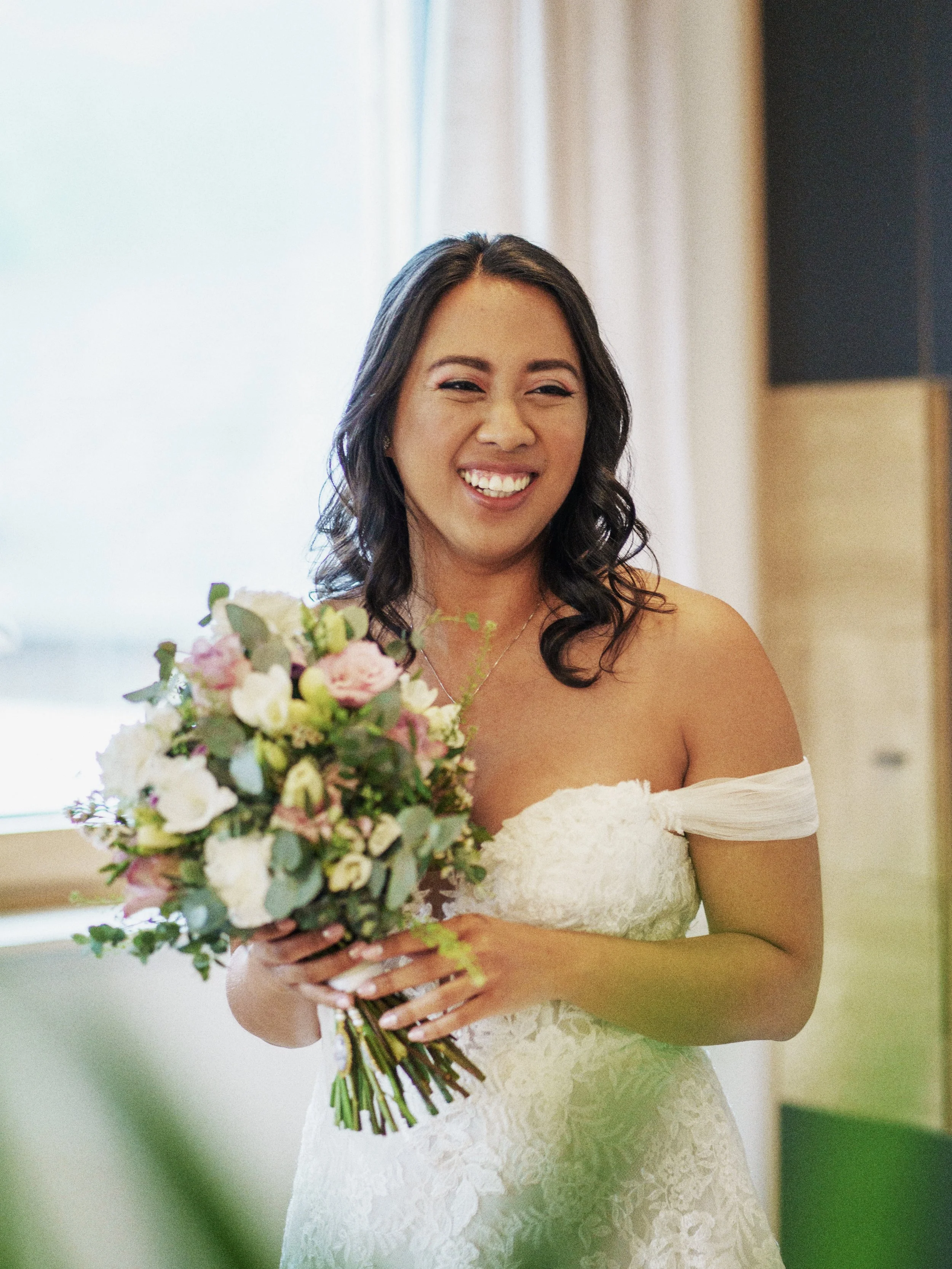 Junge Frau in Brautkleid hält einen Blumenstrauß und lächelt.