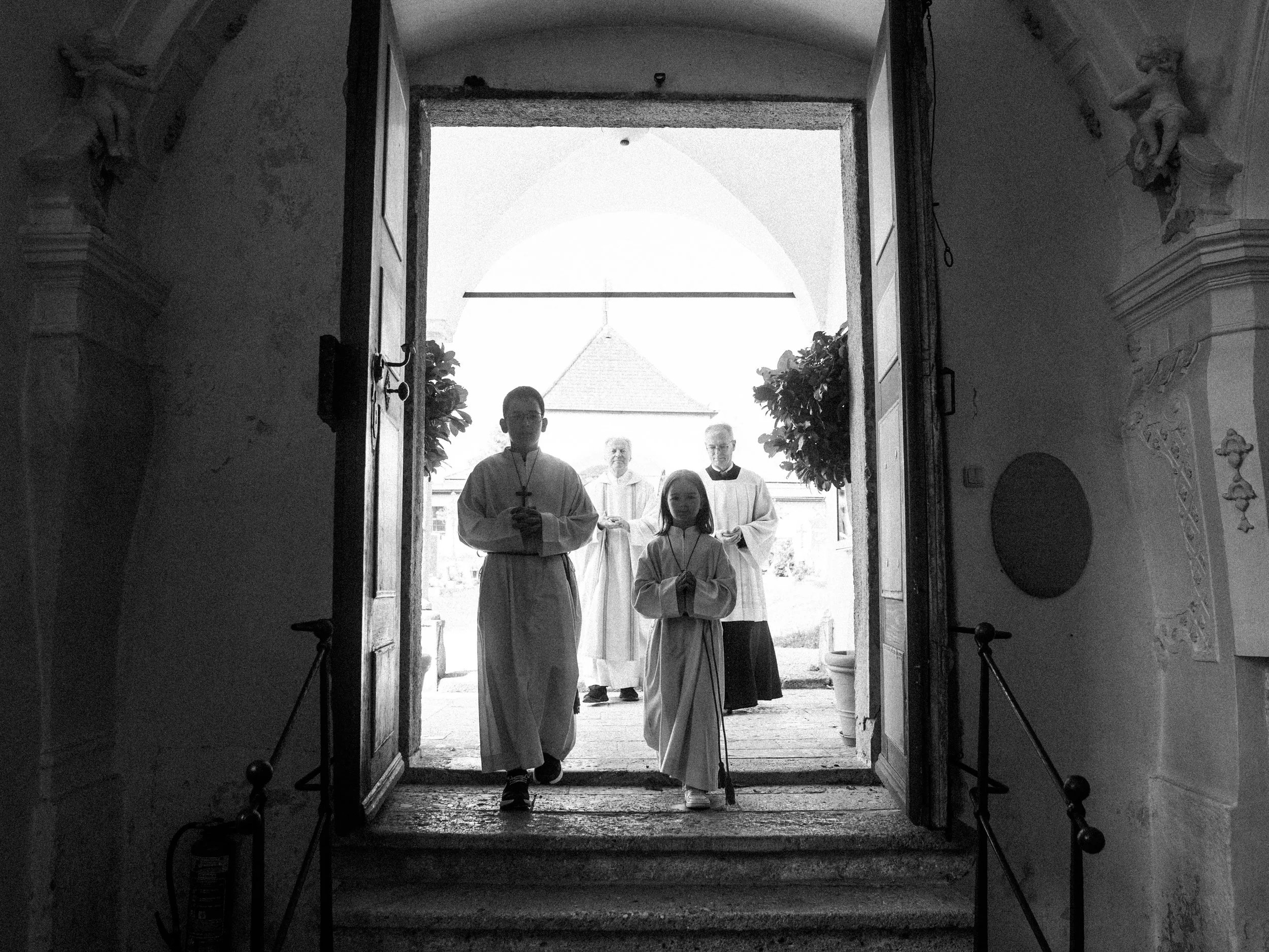 Menschen in liturgischer Kleidung, die aus einer Kirche oder Kapelle nach draußen treten, vermutlich an einer religiösen Zeremonie beteiligt.