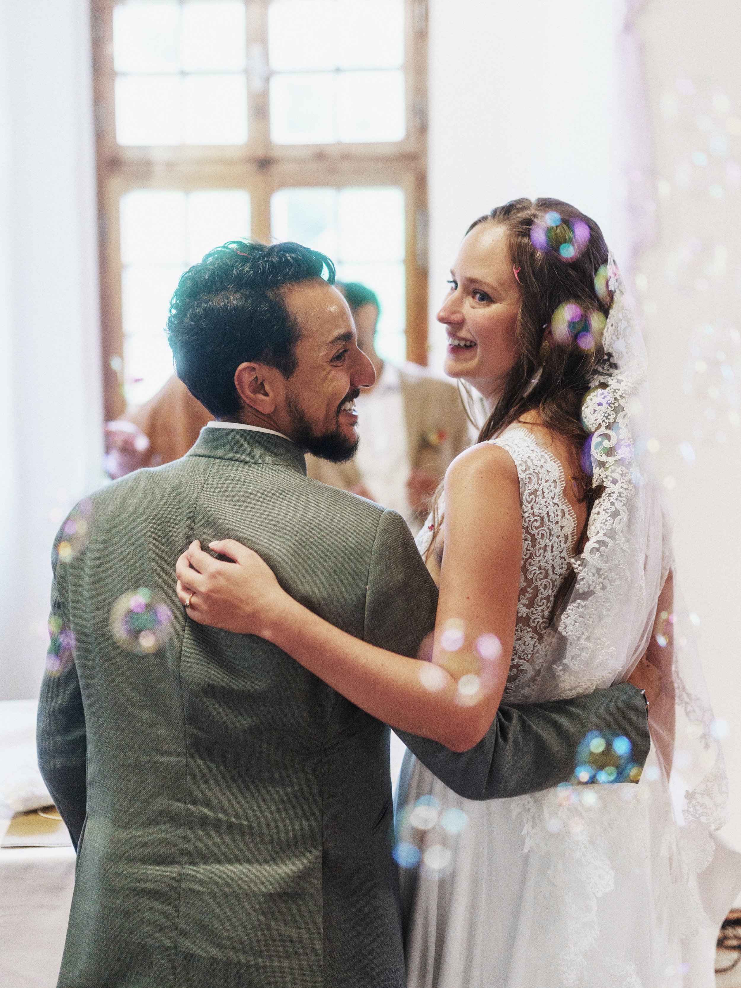 Ein Brautpaar tanzt bei einer Hochzeitsfeier, beide lachen und schauen sich an. Im Hintergrund sind weitere Gäste.