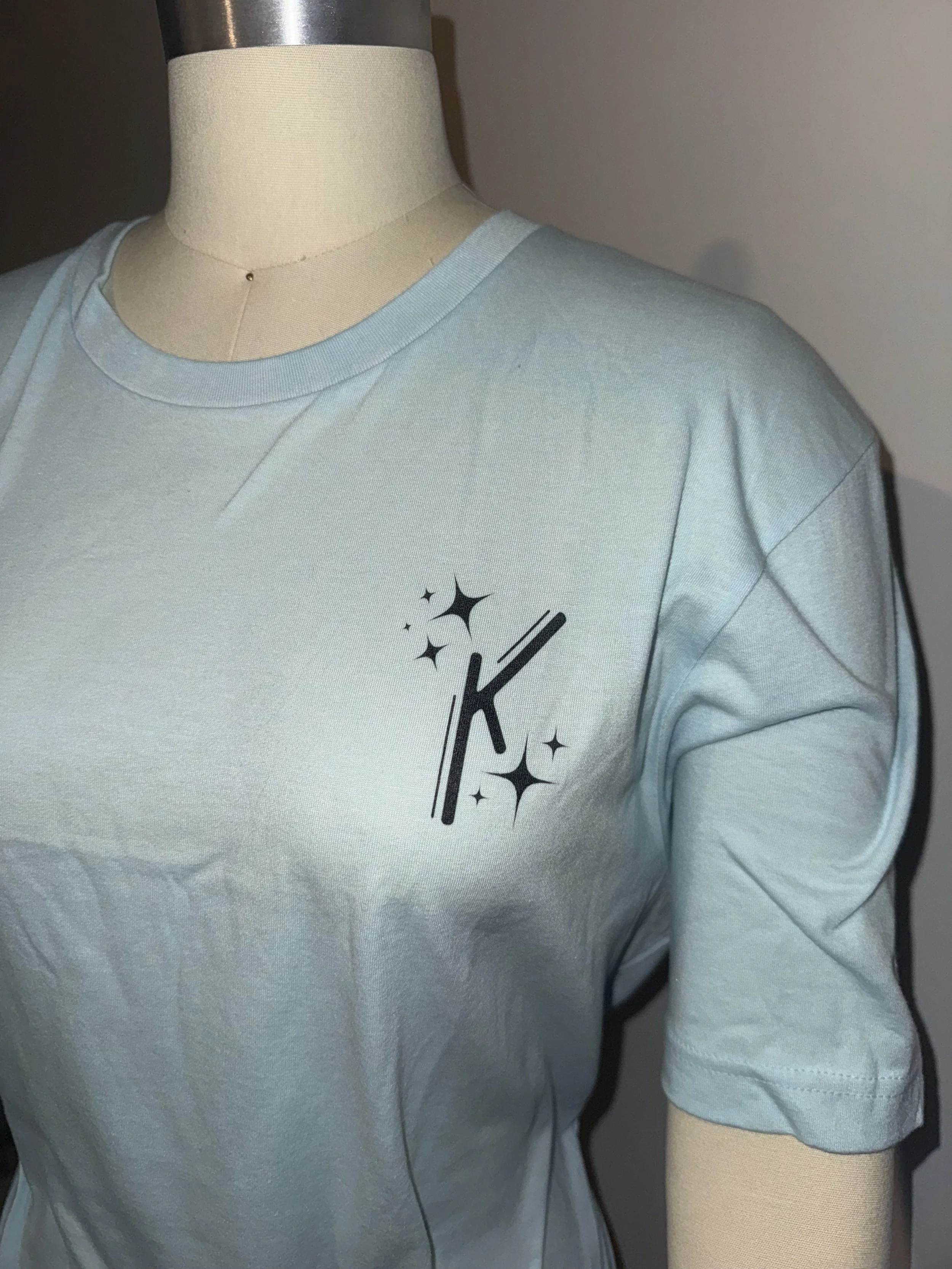 Light blue T-shirt with black 'Konstellation/K' logo and star-like graphics on the front.