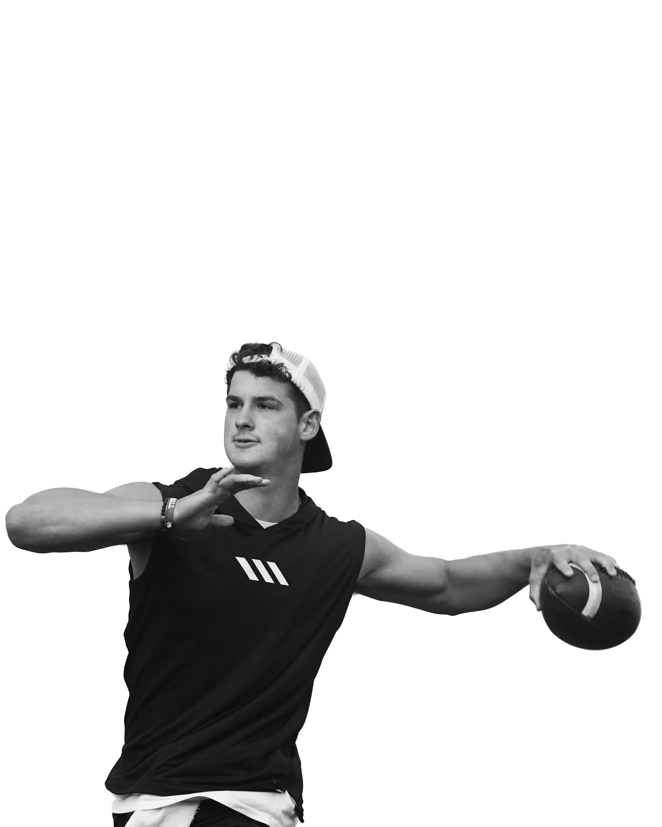 A young man wearing a sleeveless athletic shirt, baseball cap backwards, and a bracelet, holding a football in his right hand while extending his arm, with his left hand near his chin, against a plain white background.