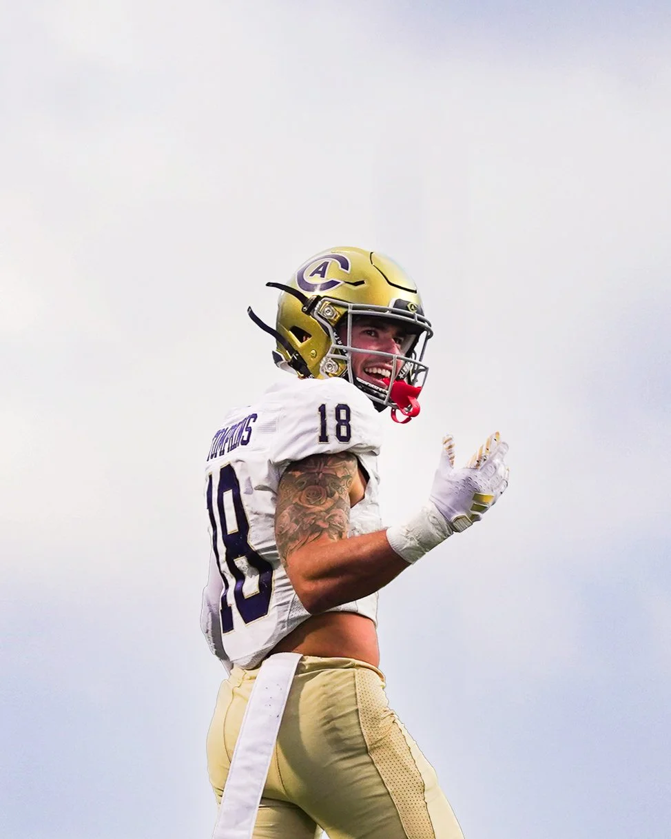 A football player wearing a white and gold uniform with the number 10, gold helmet with an 'A' logo, smiling and making a hand gesture on the field.
