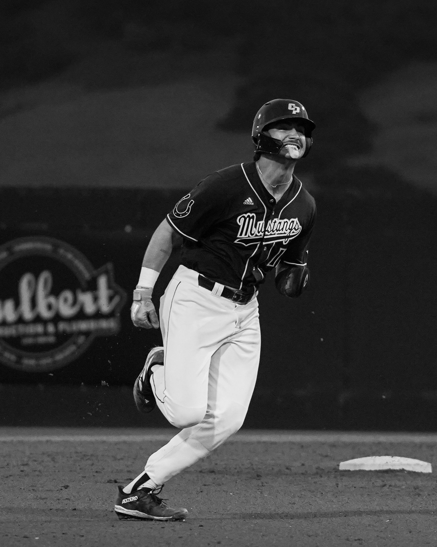 A baseball player running on the field, wearing a helmet and uniform with 'Mustangs' written on it, against a dark background.