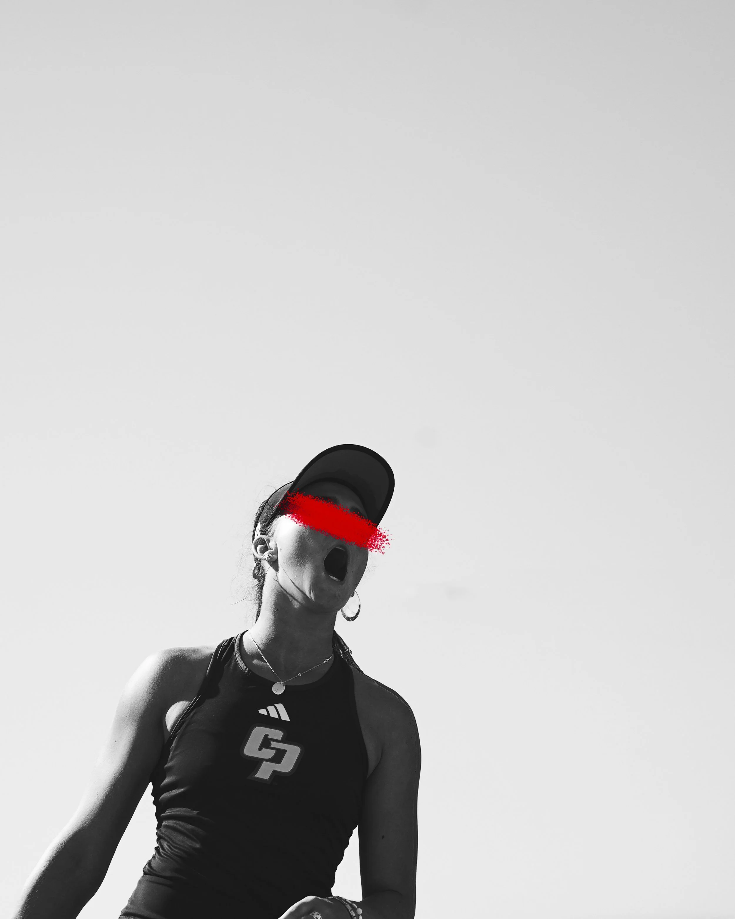 Black and white photo of a woman wearing a cap, earrings, and a sports top, with a red mark obscuring her eyes, and her mouth open as if shouting or cheering.
