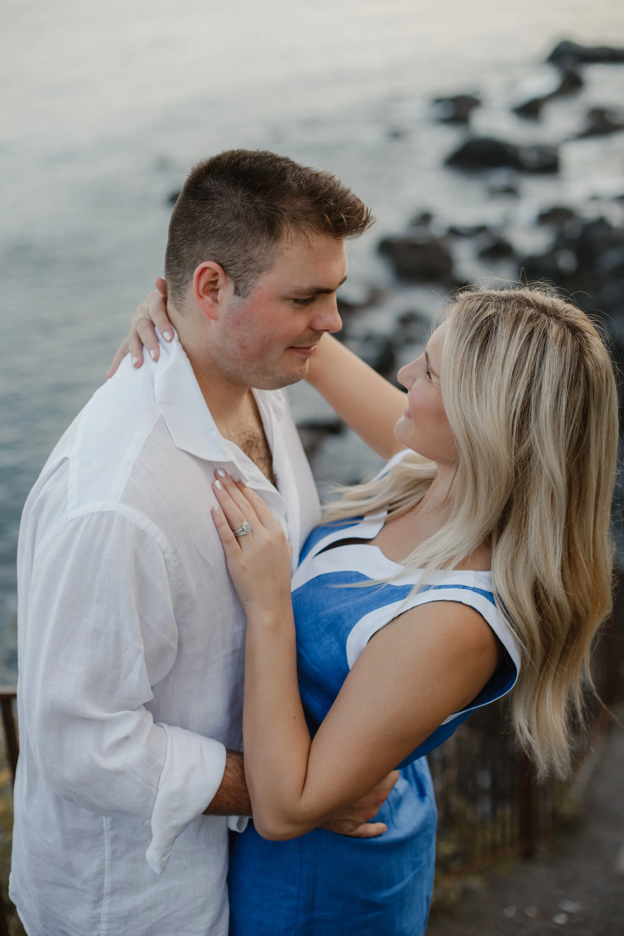 A couple standing close by the water, looking into each other's eyes with affection.