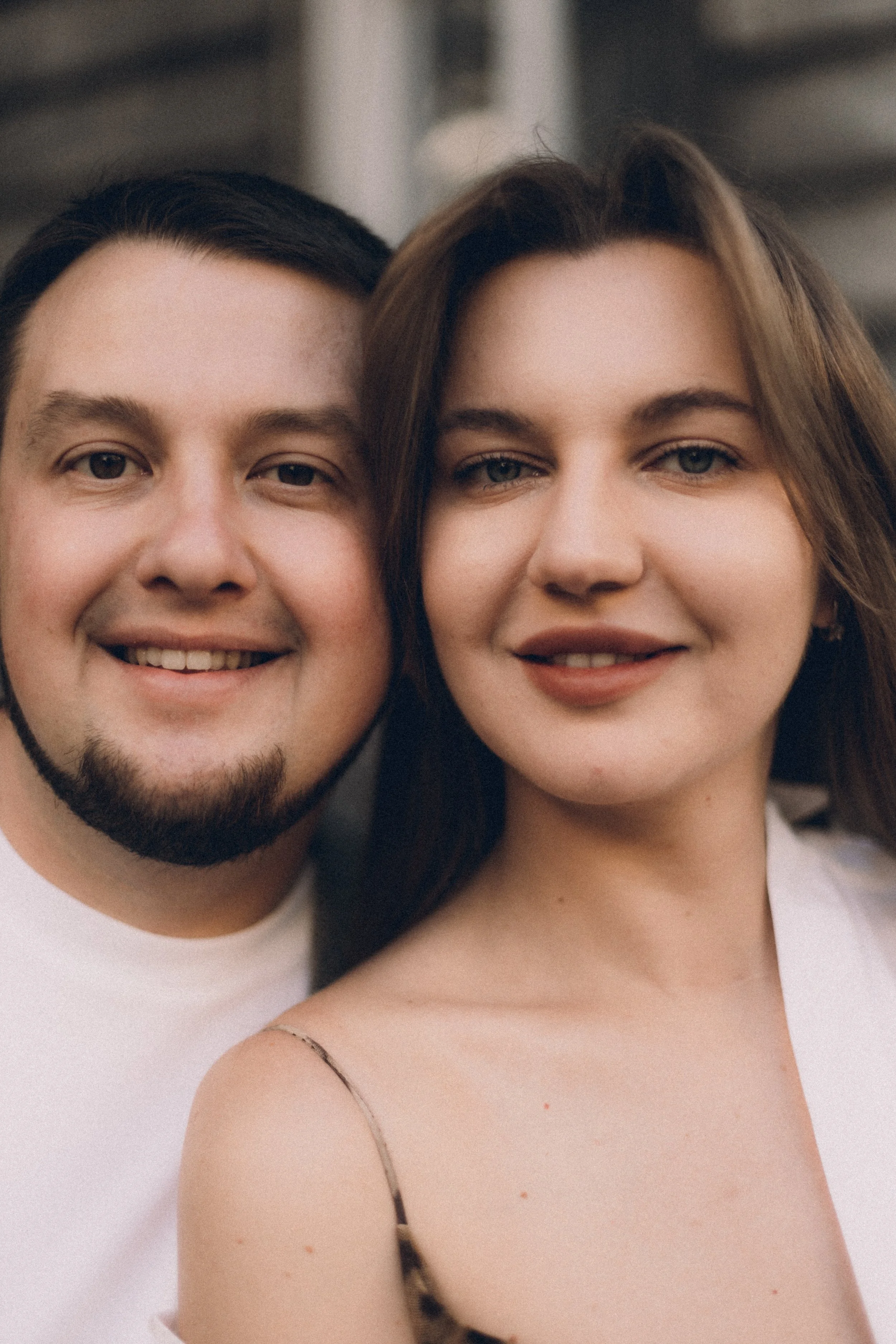 Close-up of a smiling young man and woman standing closely together, in an outdoor setting.