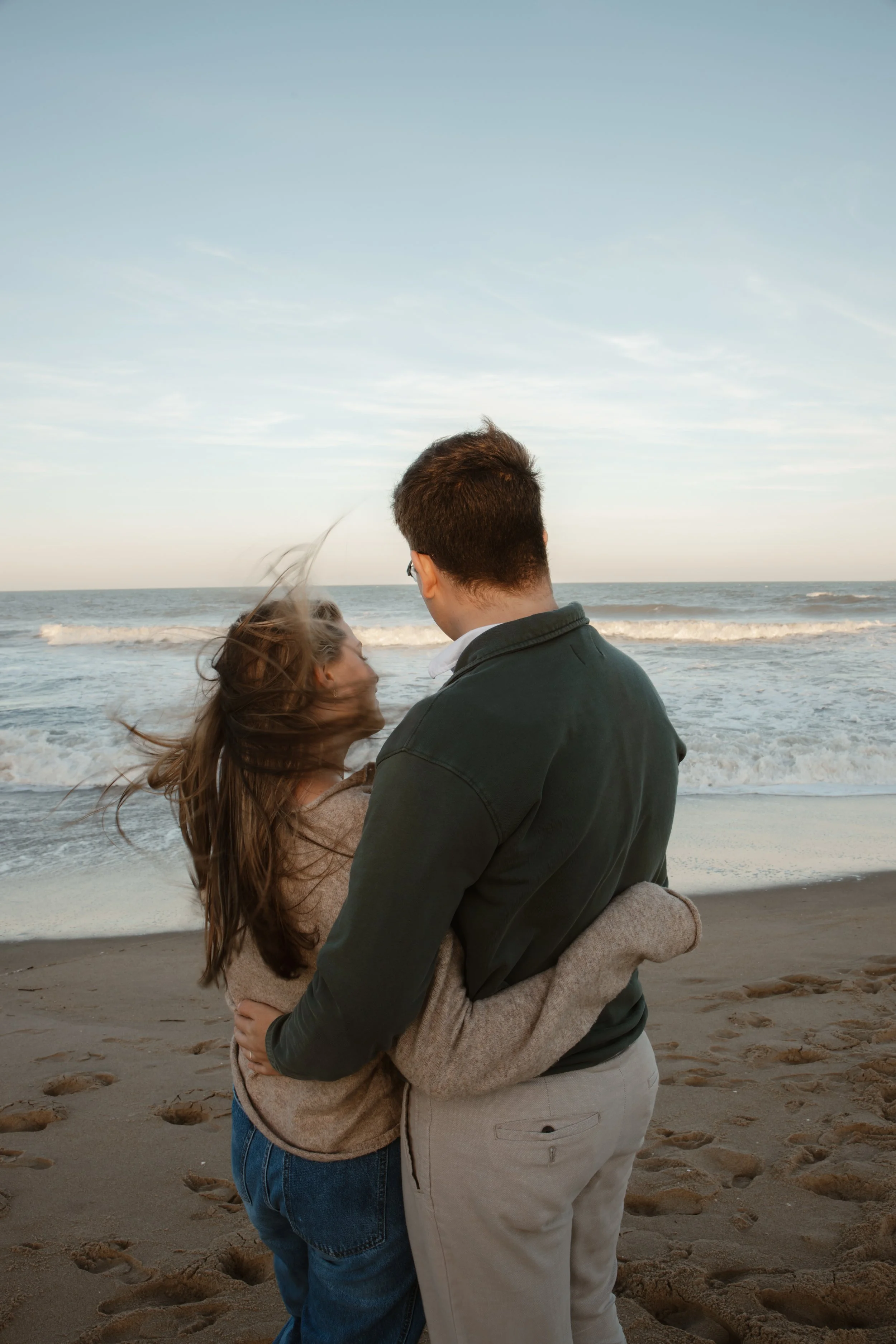 A couple embracing on the beach at sunset, with ocean waves in the background.