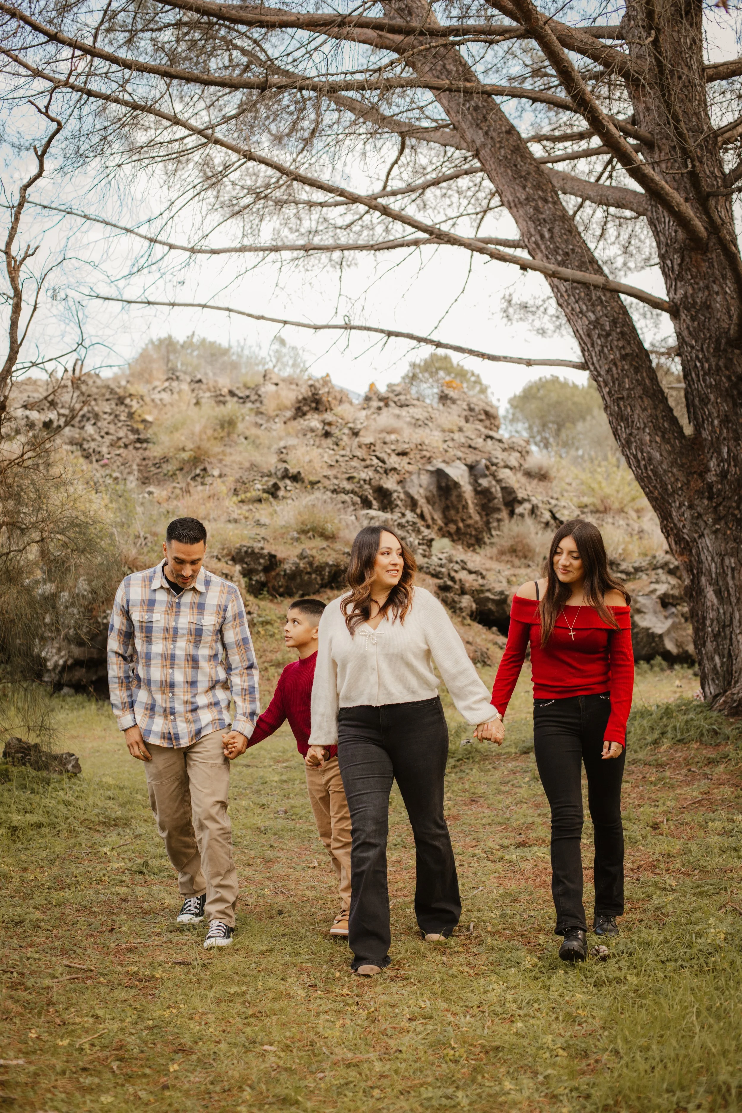 A family walking outdoors in a natural setting with trees and rocks, holding hands and enjoying each other's company.