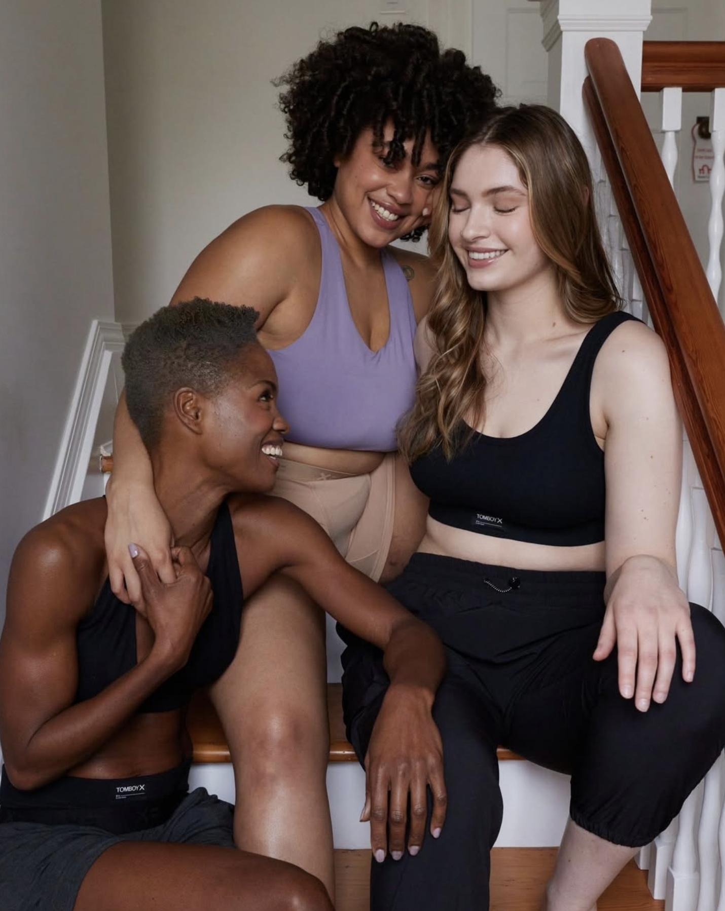 Four women sitting on stairs, smiling and hugging each other, engaging in a friendly and joyful moment.