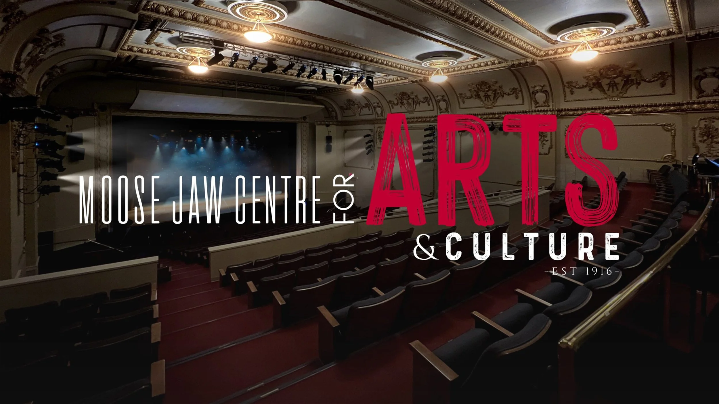 Interior view of the Moose Jaw Centre for Arts & Culture, auditorium with rows of black seats, stage with blue lighting, ornate ceiling, and decorative walls.