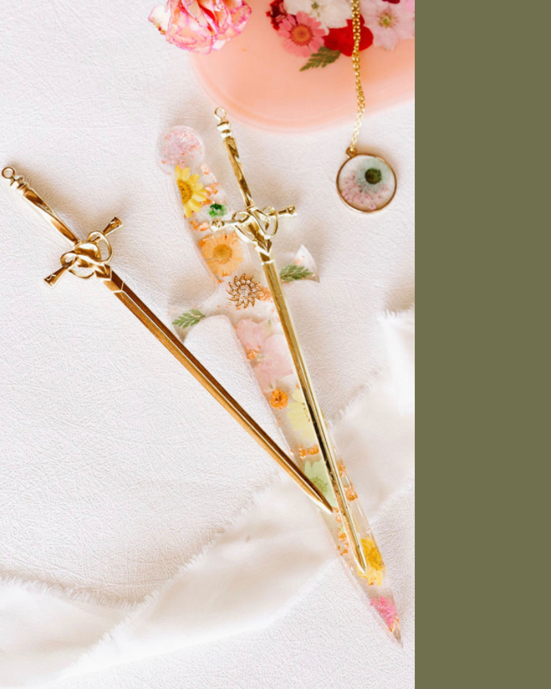 A decorative white fabric displays gold jewelry including a brooch, a pair of earrings, and a necklace with floral and colorful designs.