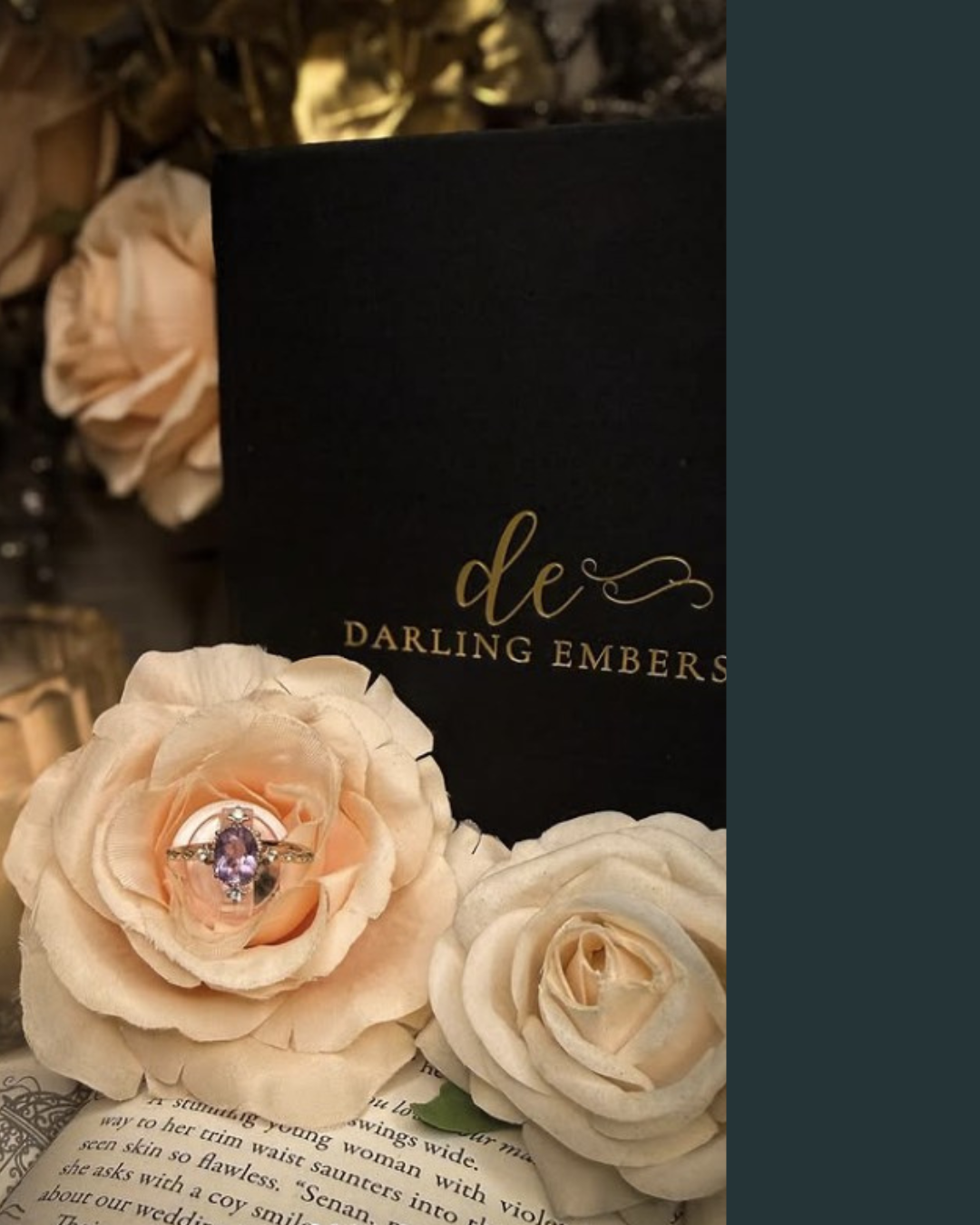 A jewelry ring with purple gemstone and diamonds, placed inside a pink rose flower. The background features a black box with "de Darling Embers" written in gold, surrounded by cream-colored roses and a page of text.