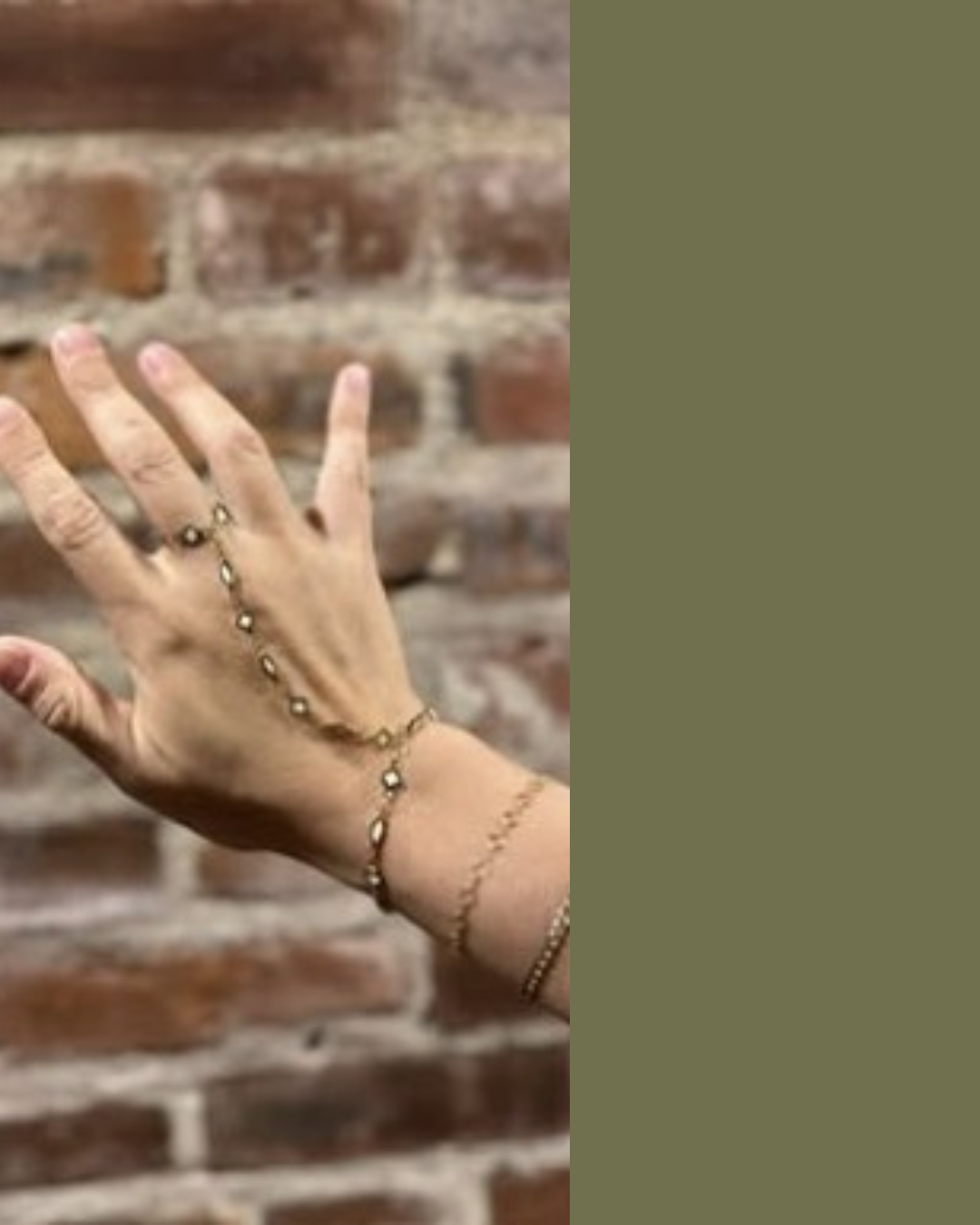 Close-up of a woman's hand and wrist adorned with delicate gold jewelry, with a brick wall in the background.