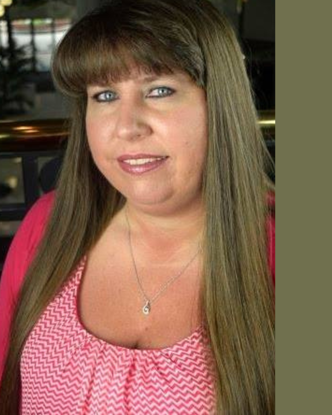A woman with long, straight, light brown hair and blue eyes, wearing a pink patterned top and a silver necklace, smiling at the camera.