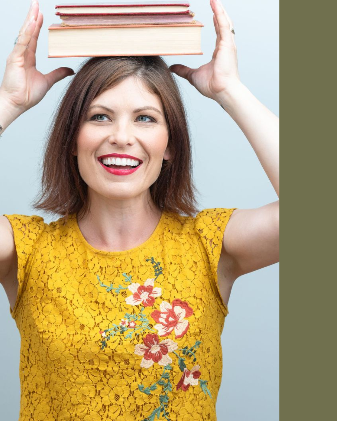 A smiling woman with shoulder-length brown hair, wearing a yellow lace dress with floral embroidery, balancing a stack of books on her head.