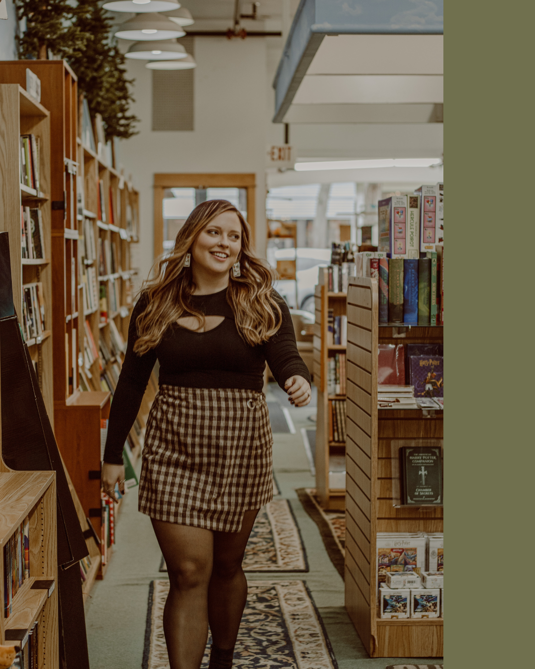 A woman walking through a bookstore aisle, smiling, with maple checkered skirt, black top, and black tights.