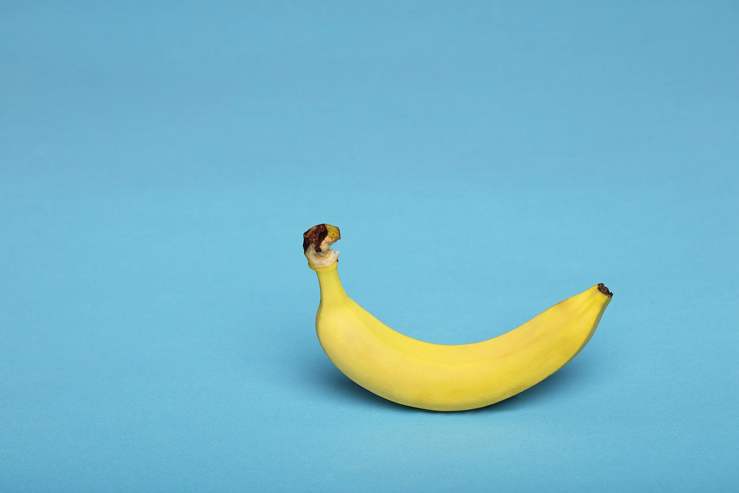 A banana with a bite taken out of its top, positioned on a bright blue background.