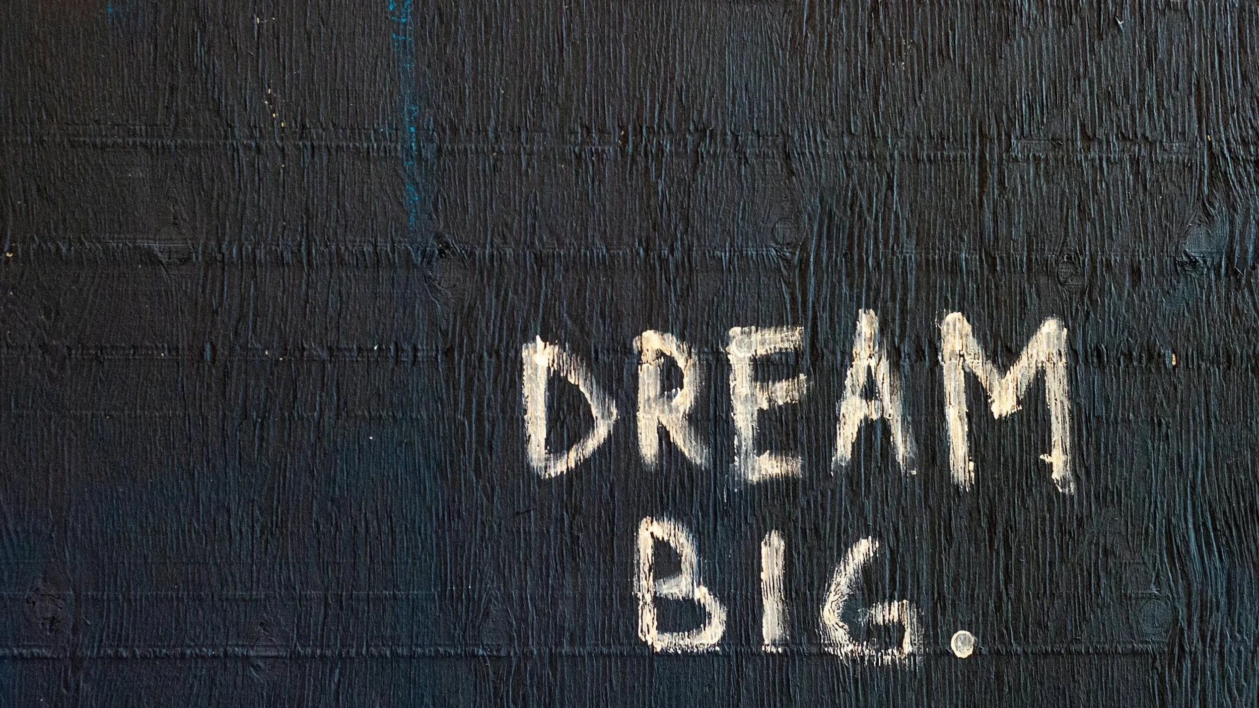 A black textured wall with the words 'DREAM BIG.' written in white chalk.