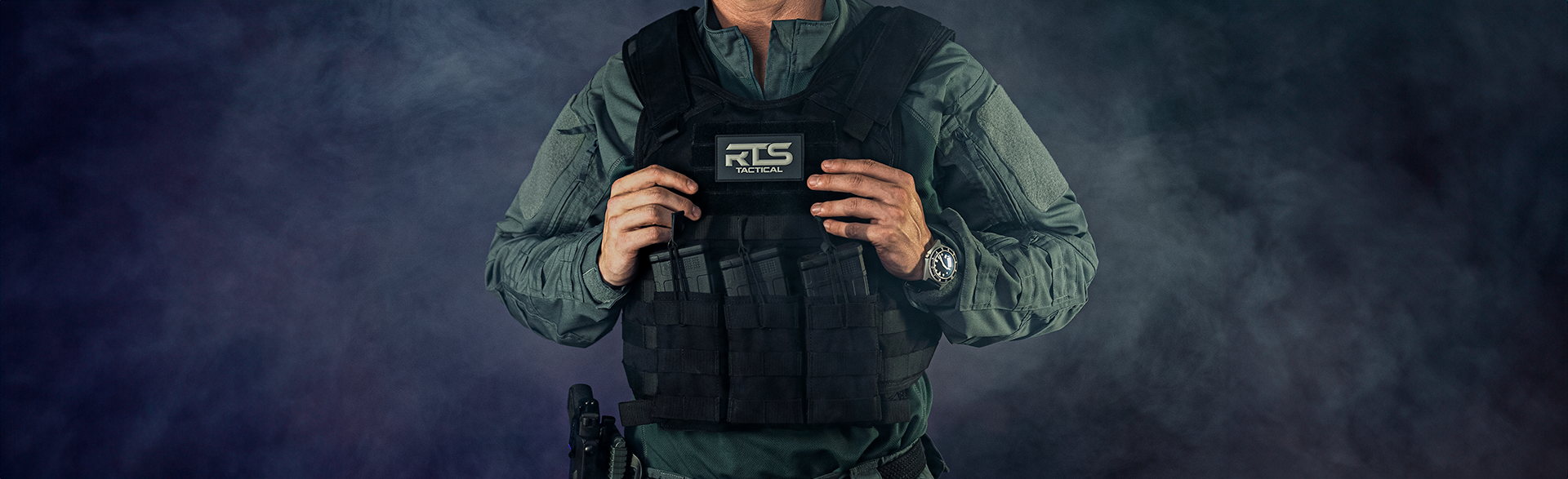 A person wearing tactical gear, including a black tactical vest with the label 'RTS Tactical,' adjusting the vest with both hands, against a dark smoky background.