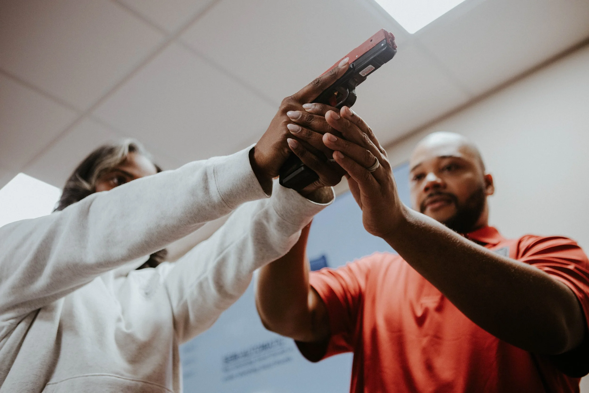 Two people holding a firearm together in an indoor setting.