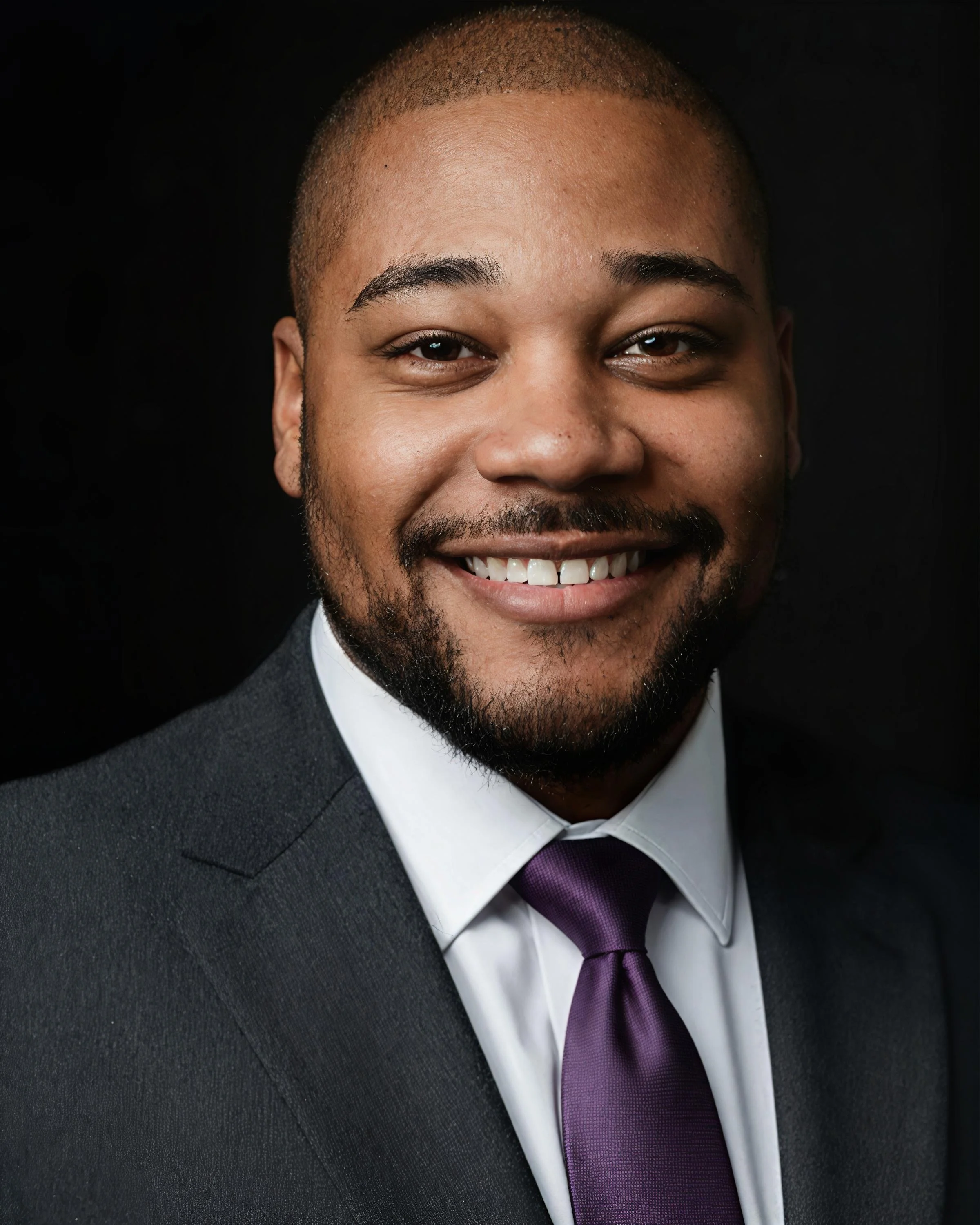 Portrait of a smiling man in a suit with a purple tie, dark background.