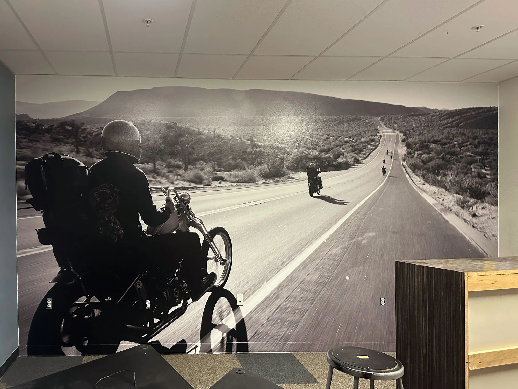 Black and white mural of motorcyclists riding on a desert highway with mountains in background.