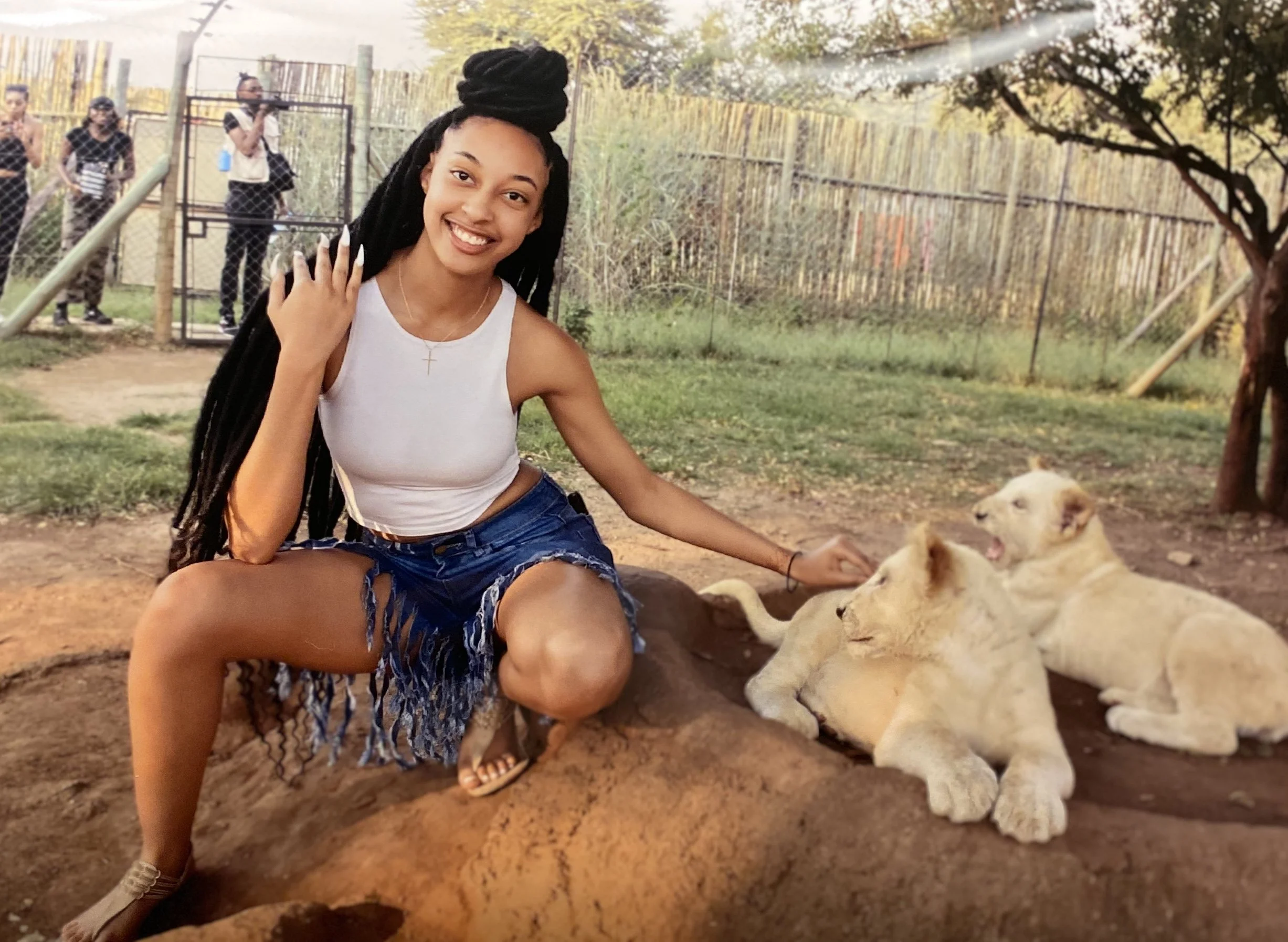 A woman kneeling on the ground with three lion cubs, smiling and petting them at a zoo or wildlife park.